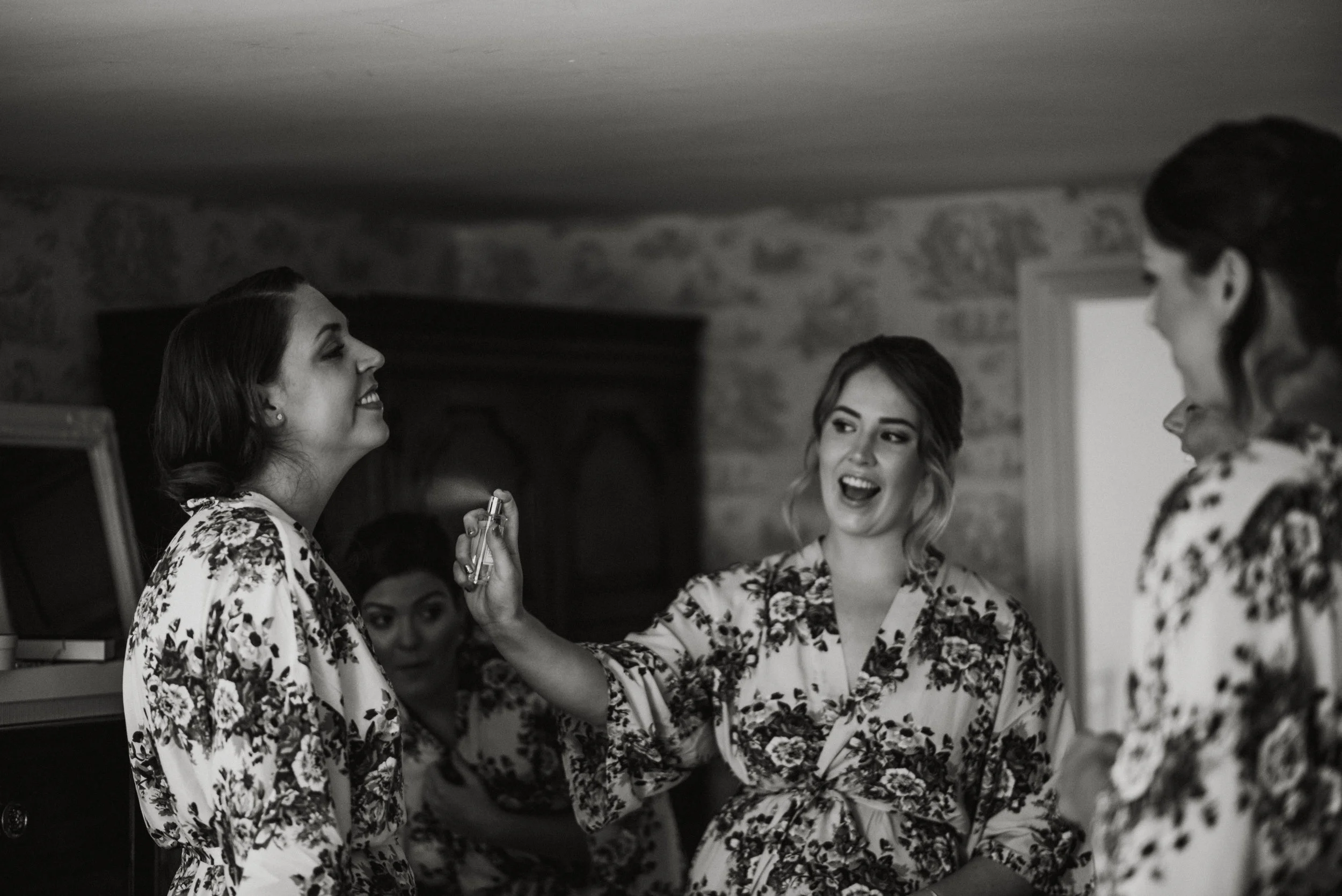 Women in floral robes smiling and laughing together in a room, possibly getting ready for a special event.