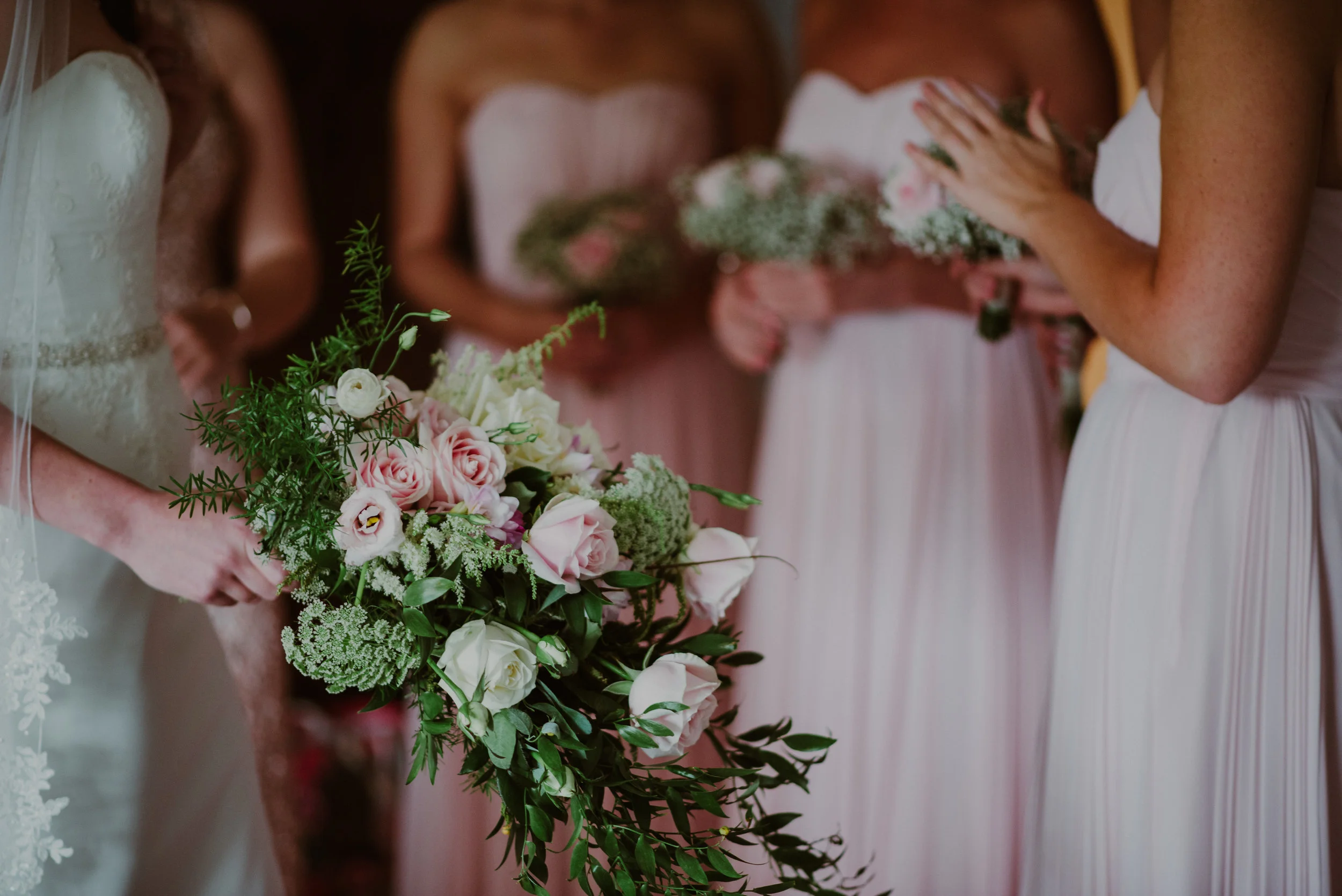 Brides holding bouquets, with pink and white roses, at a wedding.