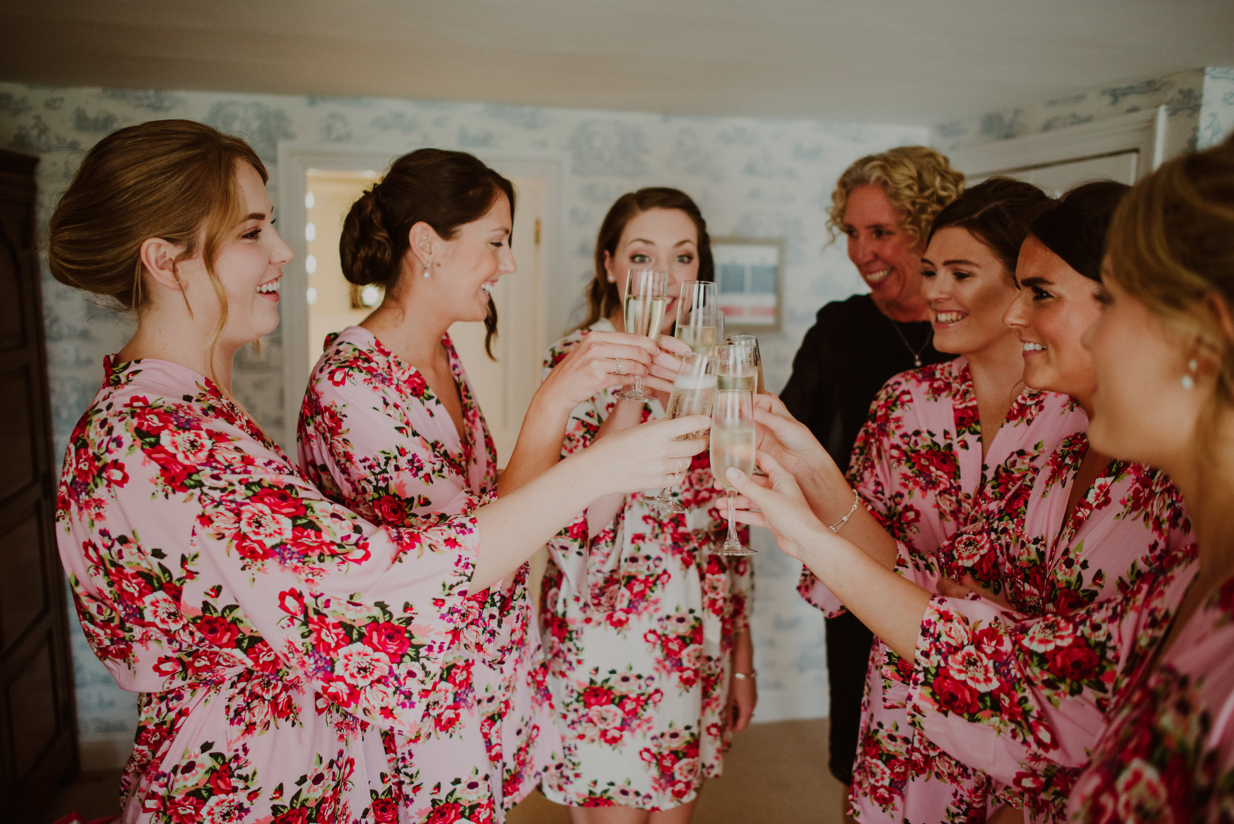 Women in matching floral robes toasting with champagne glasses during a celebration.