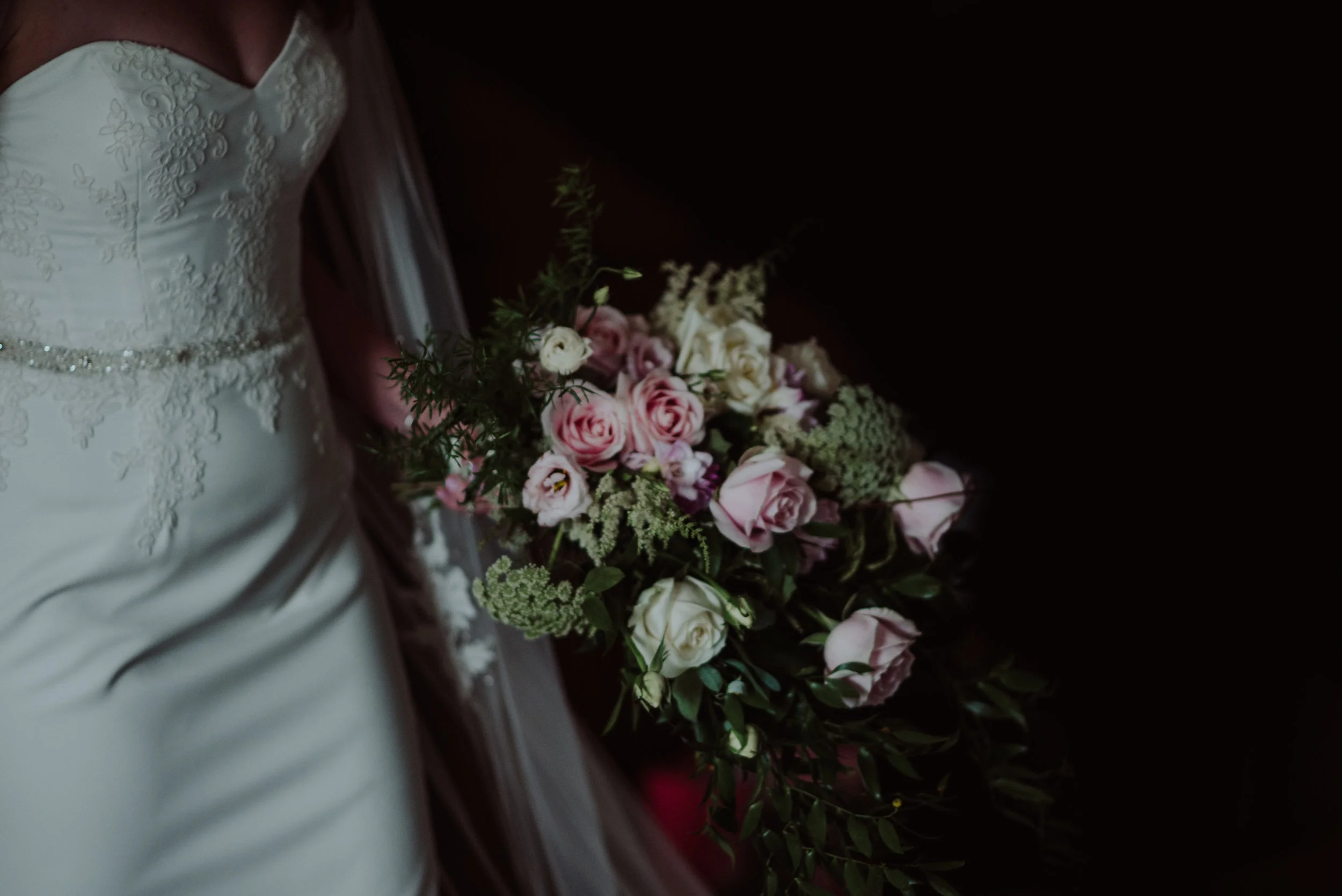 Bride in a white wedding dress holding a bouquet of pink and white roses with greenery.