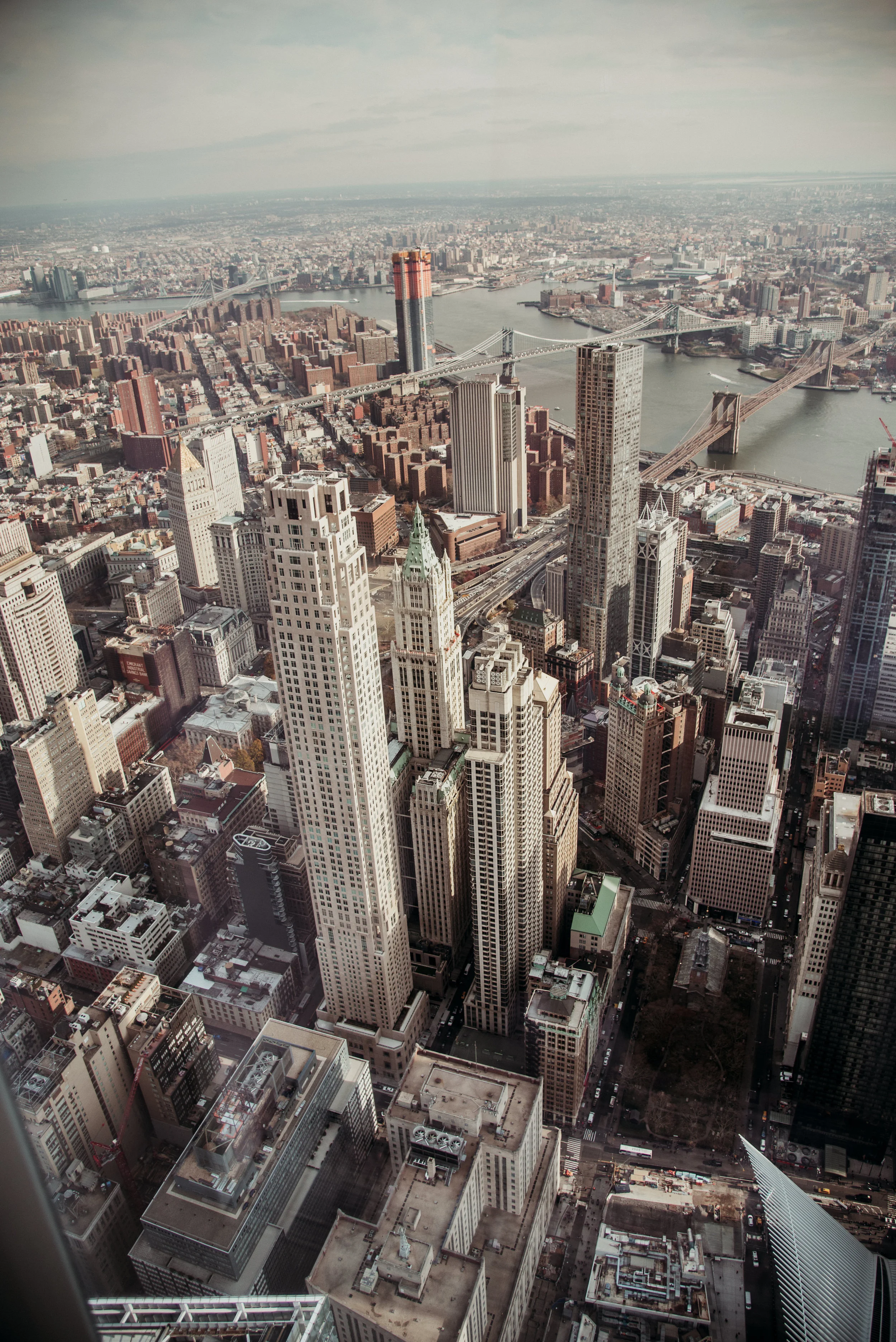 Aerial view of New York City skyline with tall skyscrapers, bridges over the river, and dense urban buildings.