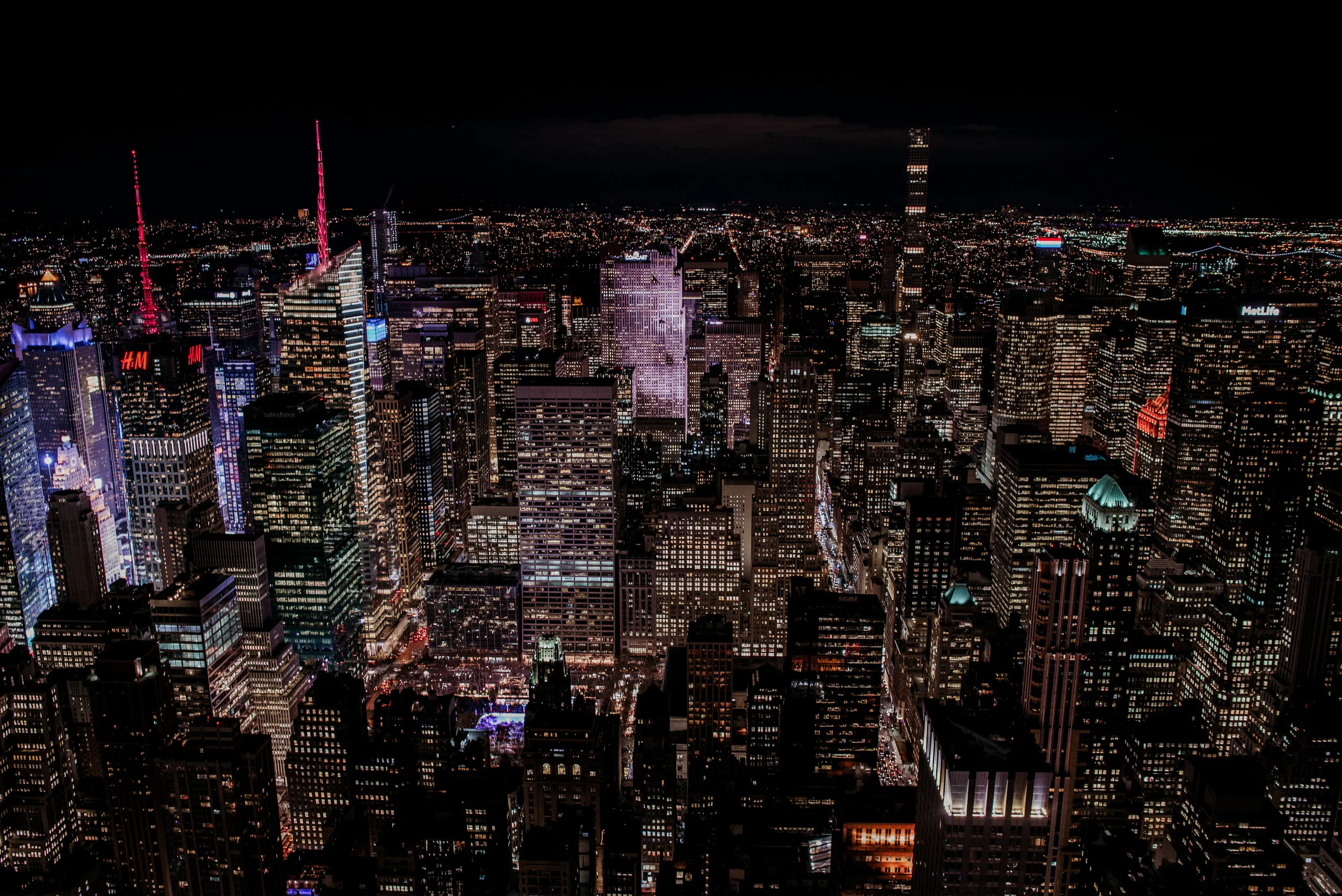 Nighttime aerial view of New York City skyline filled with illuminated skyscrapers and buildings, with streets below.