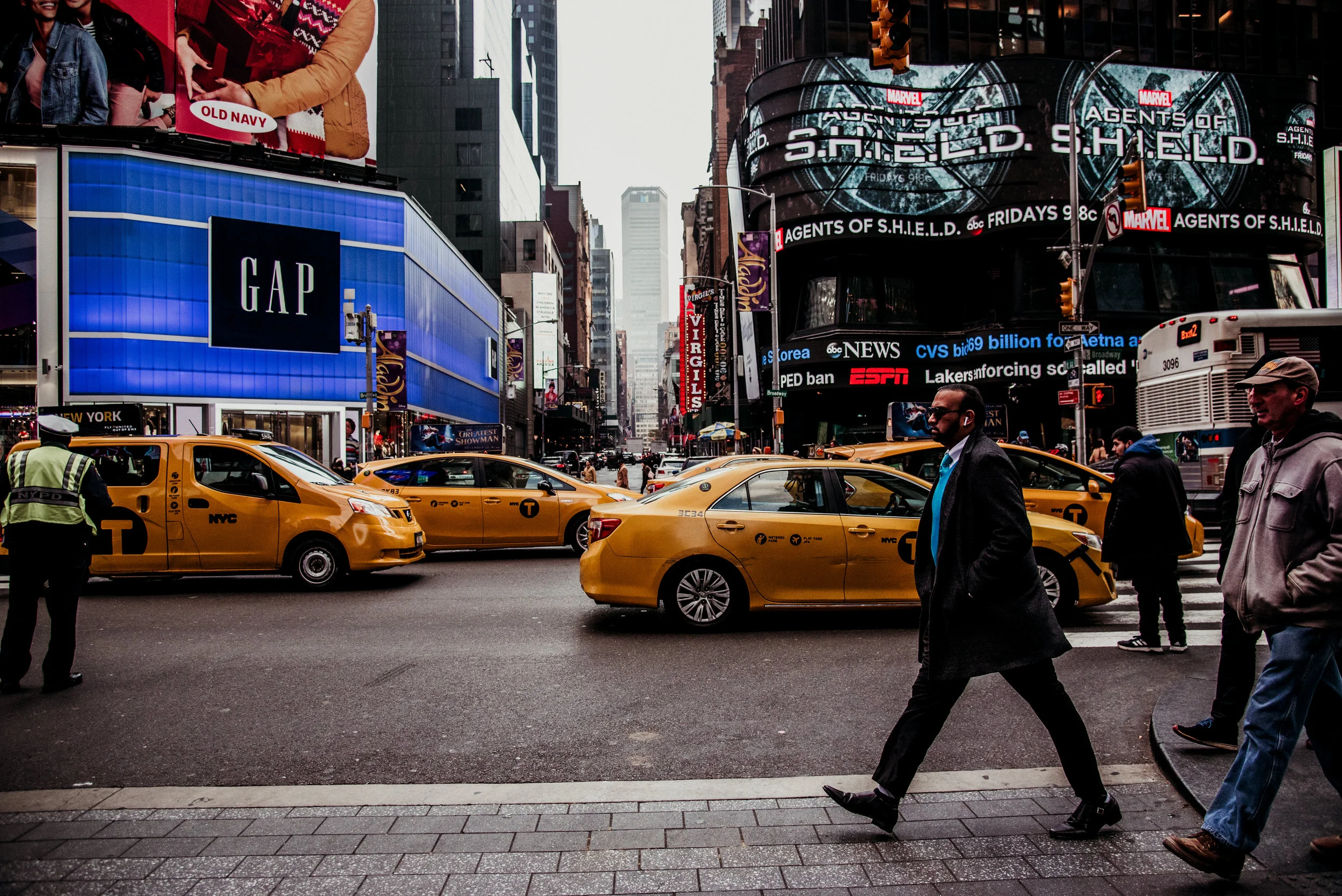 City street scene in Times Square, New York City, with yellow taxis, pedestrians, and digital billboards advertising Marvel's Agent of S.H.I.E.L.D.