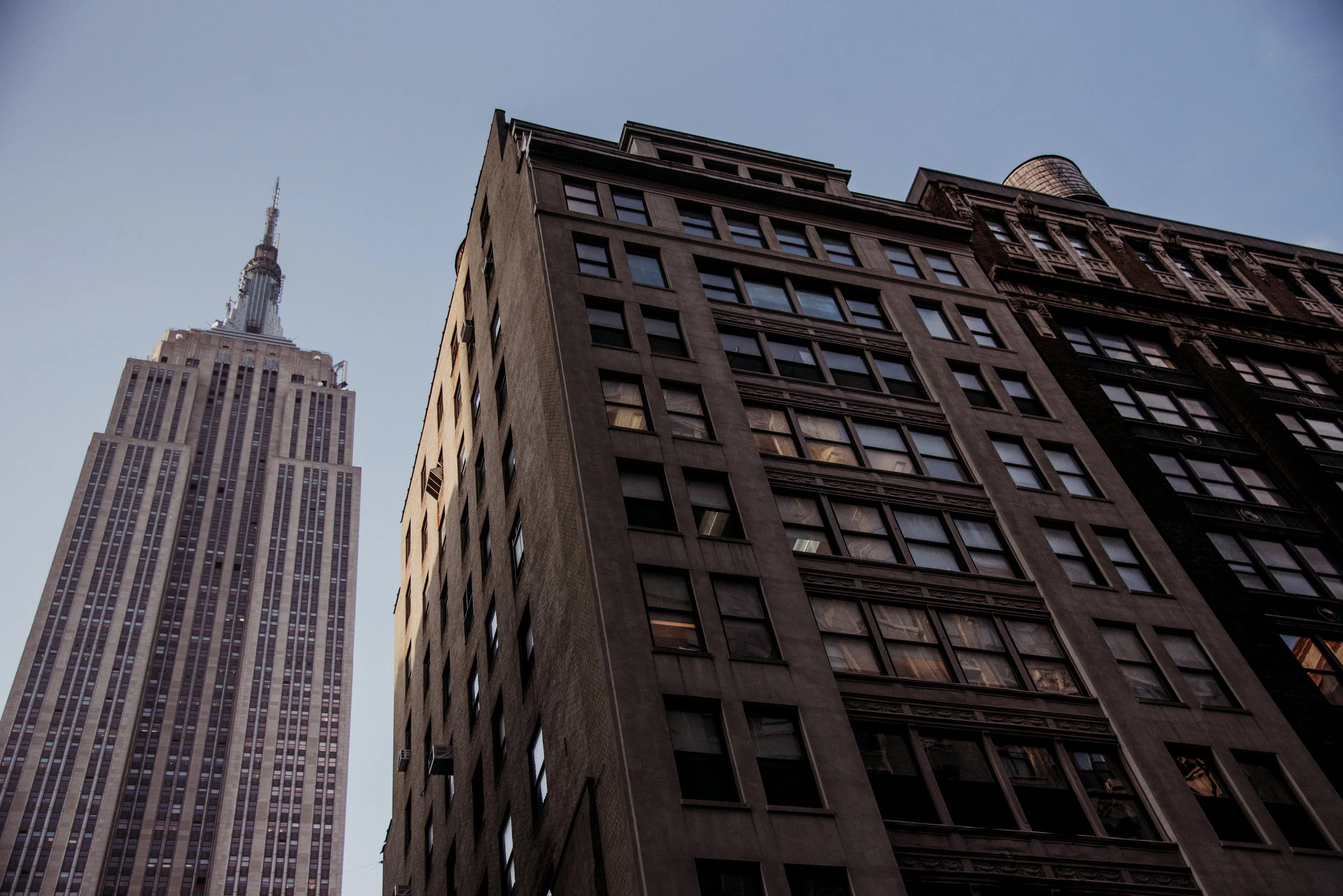 View of skyscrapers in New York City, including the Empire State Building, seen from a low angle during dusk.