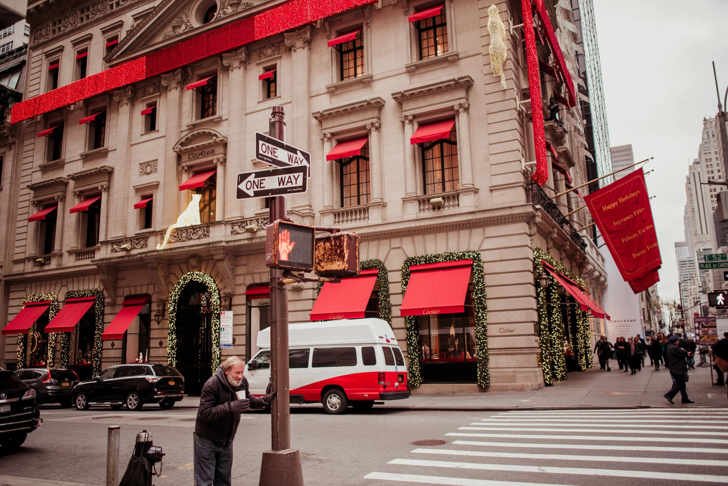 A corner building decorated with red and gold holiday ornaments and lights, with a Cartier store on the ground floor, street signs, and pedestrians.
