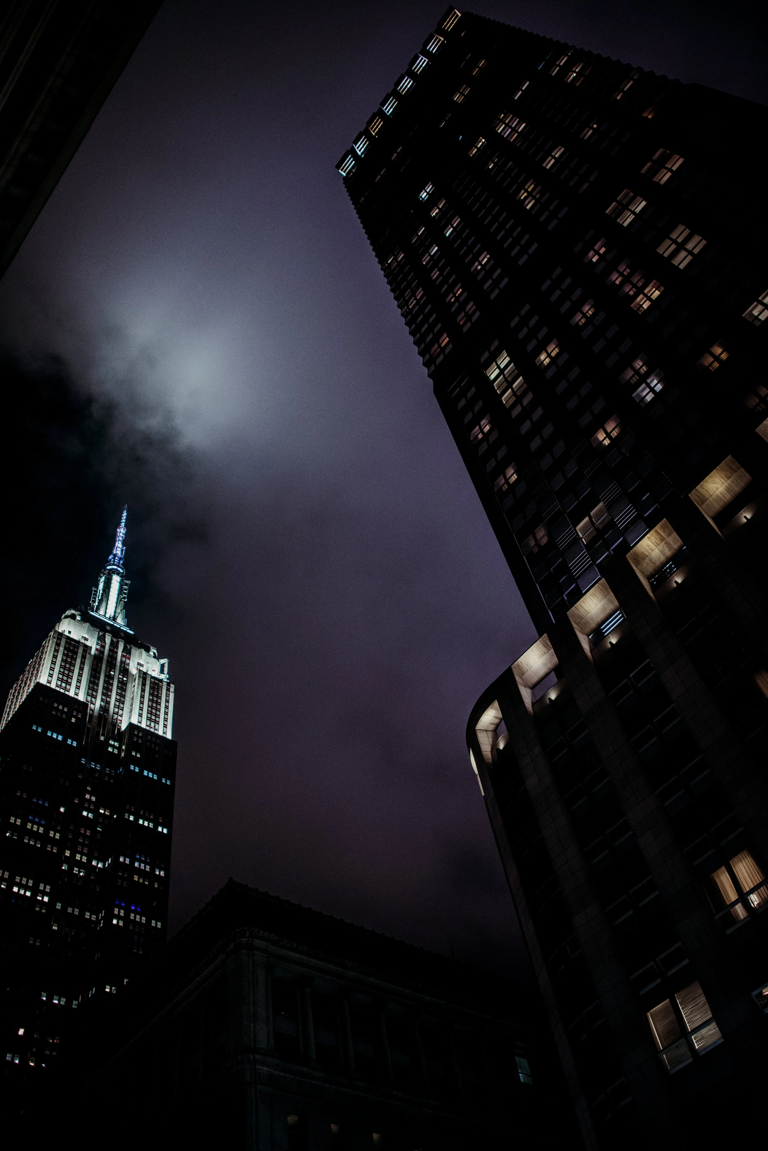 Nighttime cityscape with illuminated skyscrapers, including the Empire State Building, viewed from a low angle.