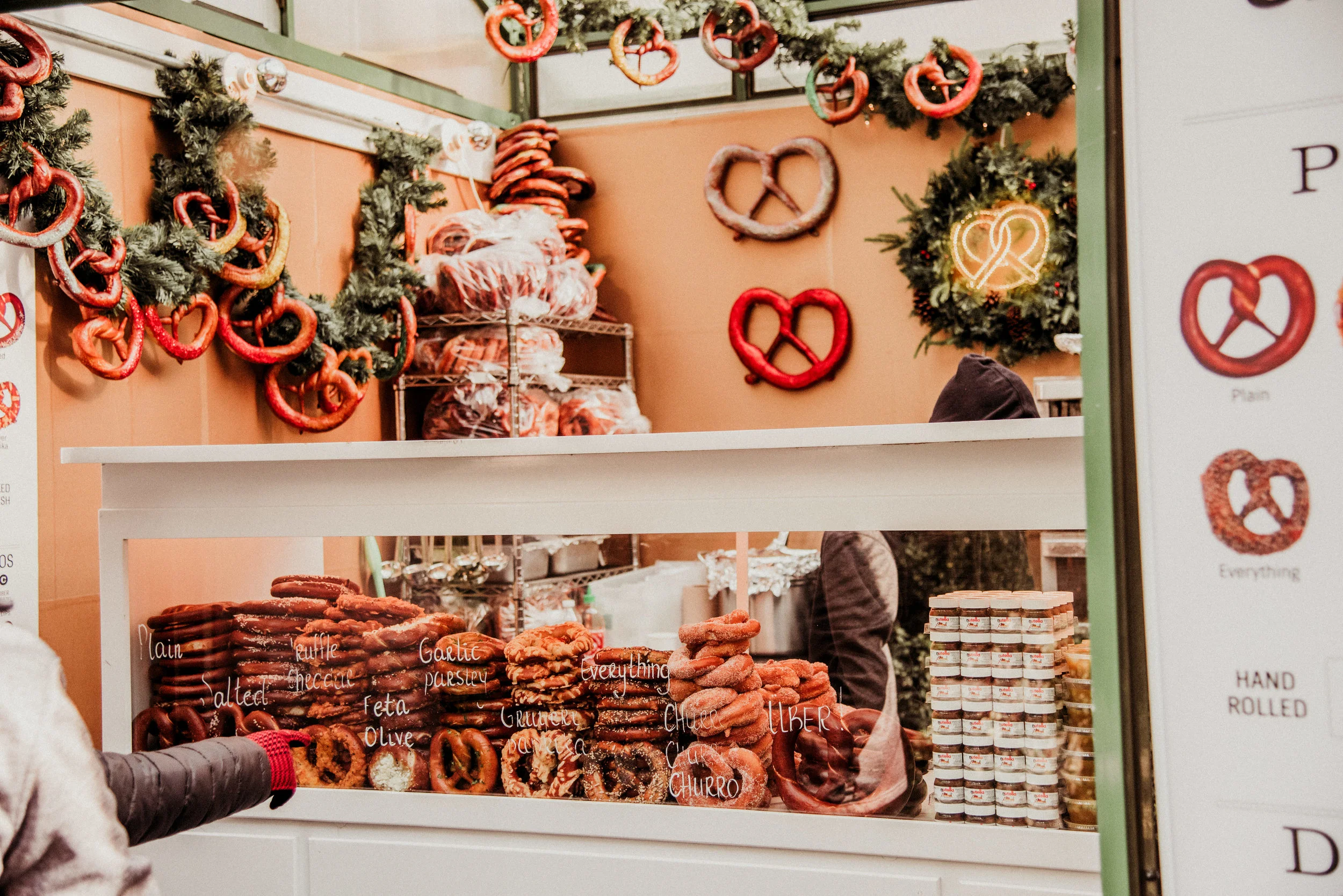 A festive display of various pretzels and baked goods in a bakery stall decorated with holiday wreaths and ornaments.