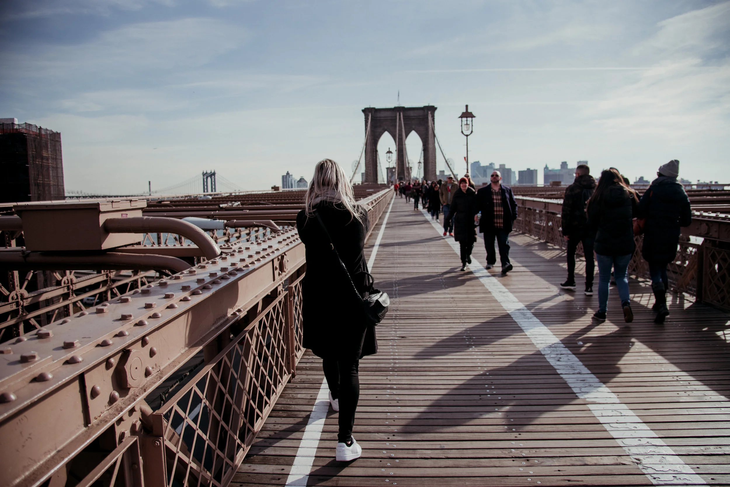 People walking on the Brooklyn Bridge in New York City on a sunny day.