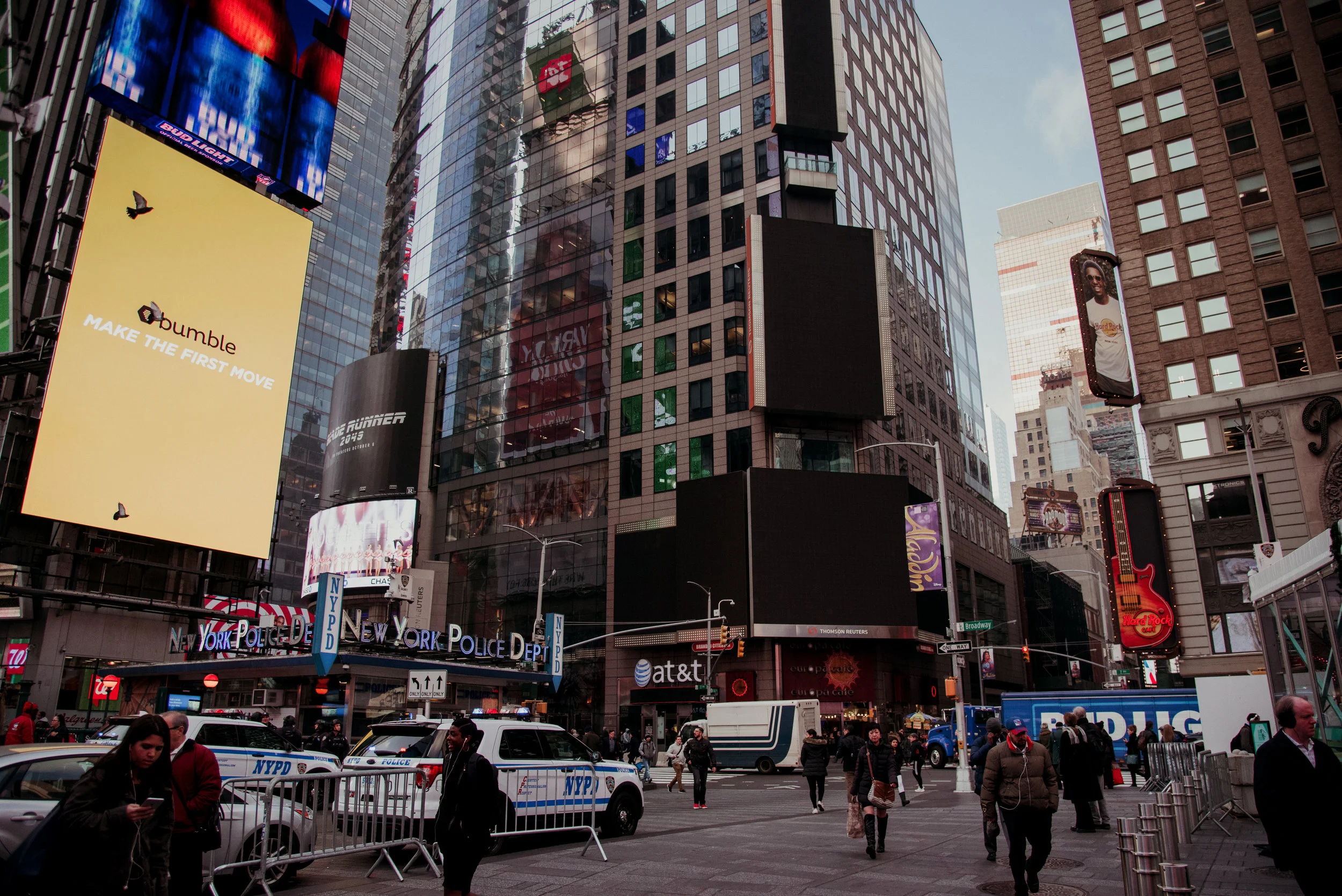 Busy city intersection in Times Square, New York City, with tall buildings, digital billboards, police cars, and pedestrians.