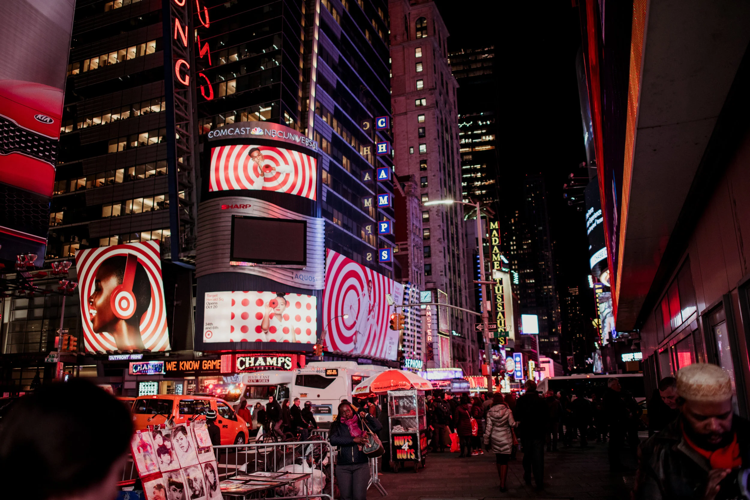 People walking in Times Square at night with bright billboards and neon signs.