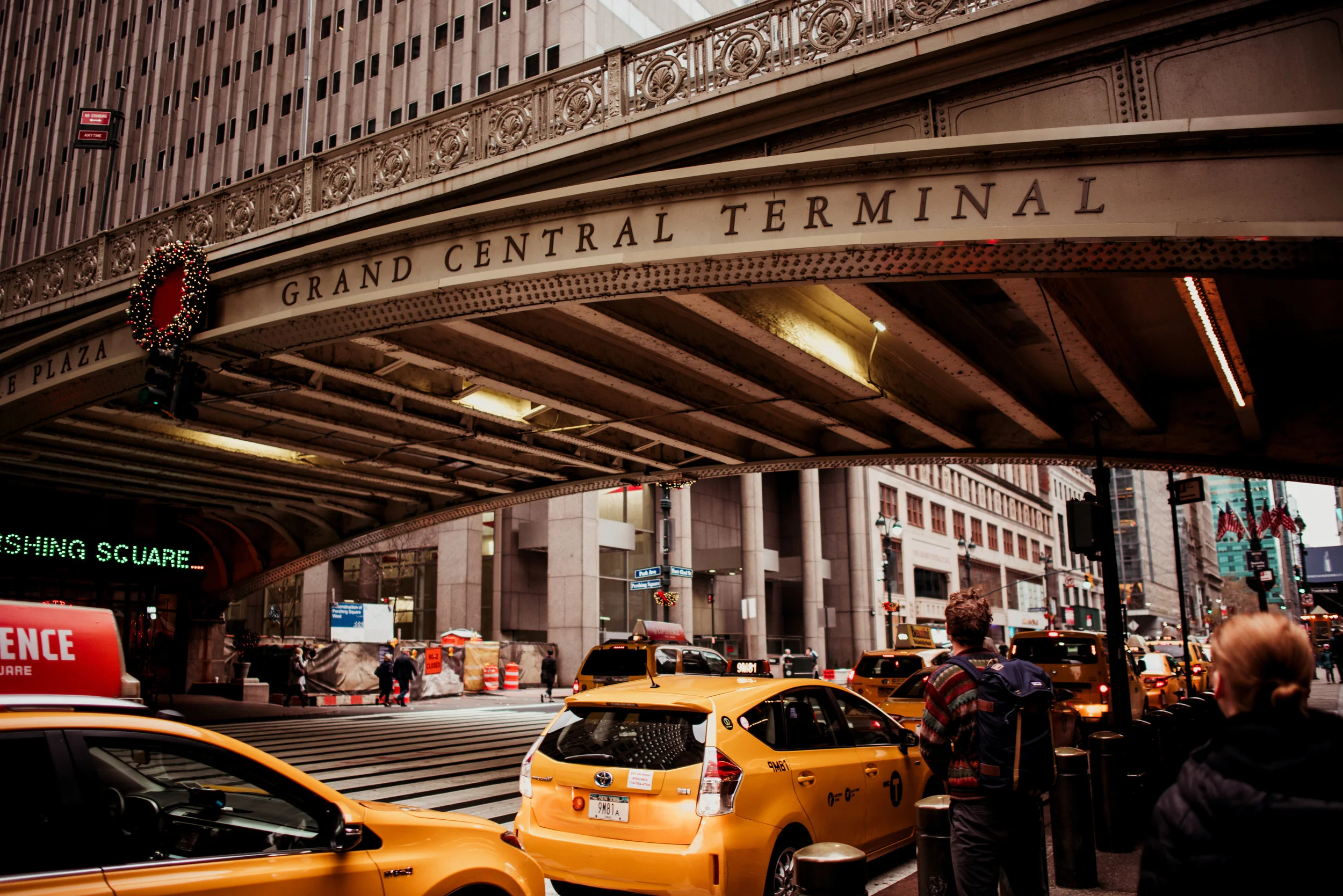 Yellow taxis on a city street under a bridge with the sign 'Grand Central Terminal' in New York City.