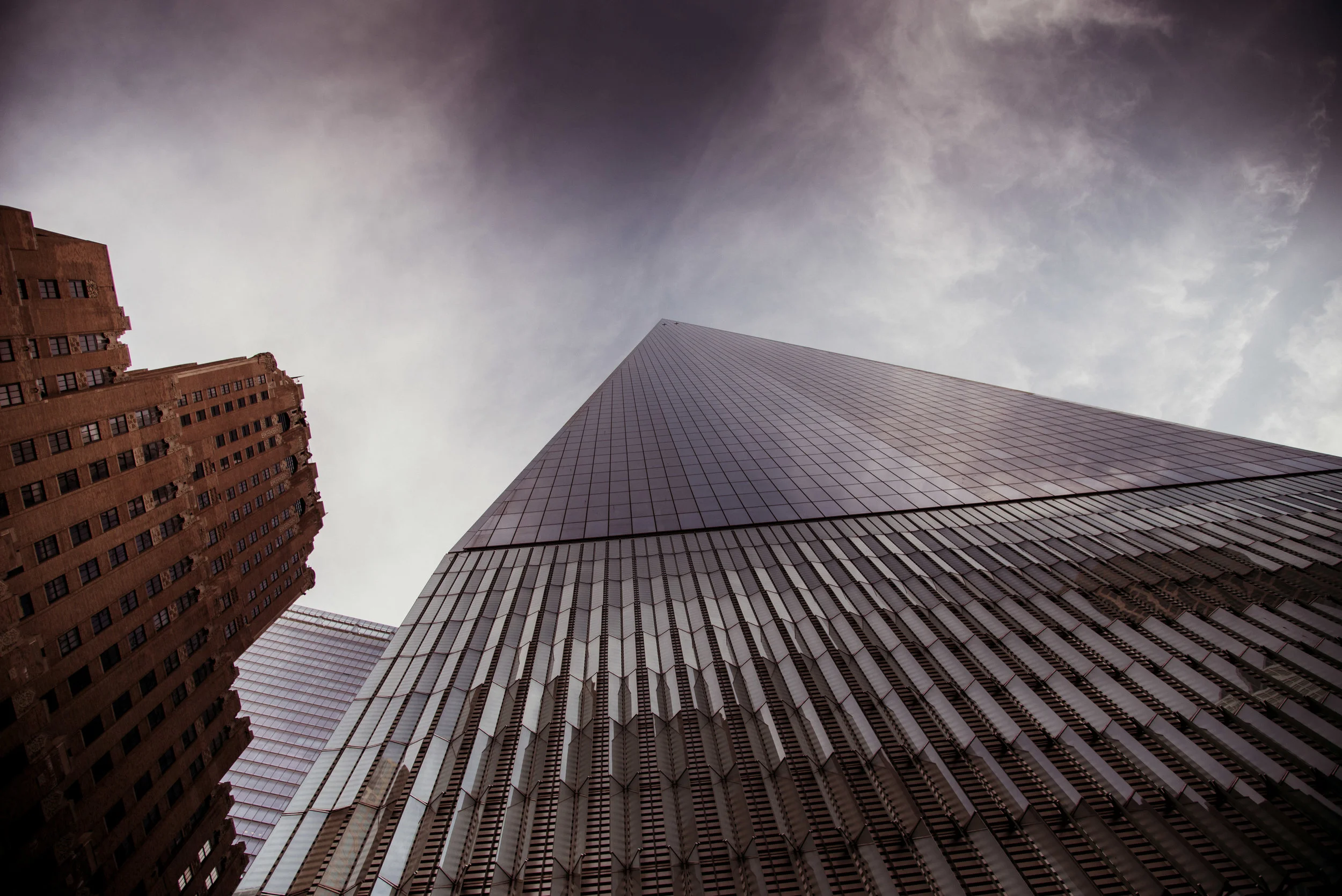 Looking up at tall skyscrapers with glass facades against a cloudy sky.