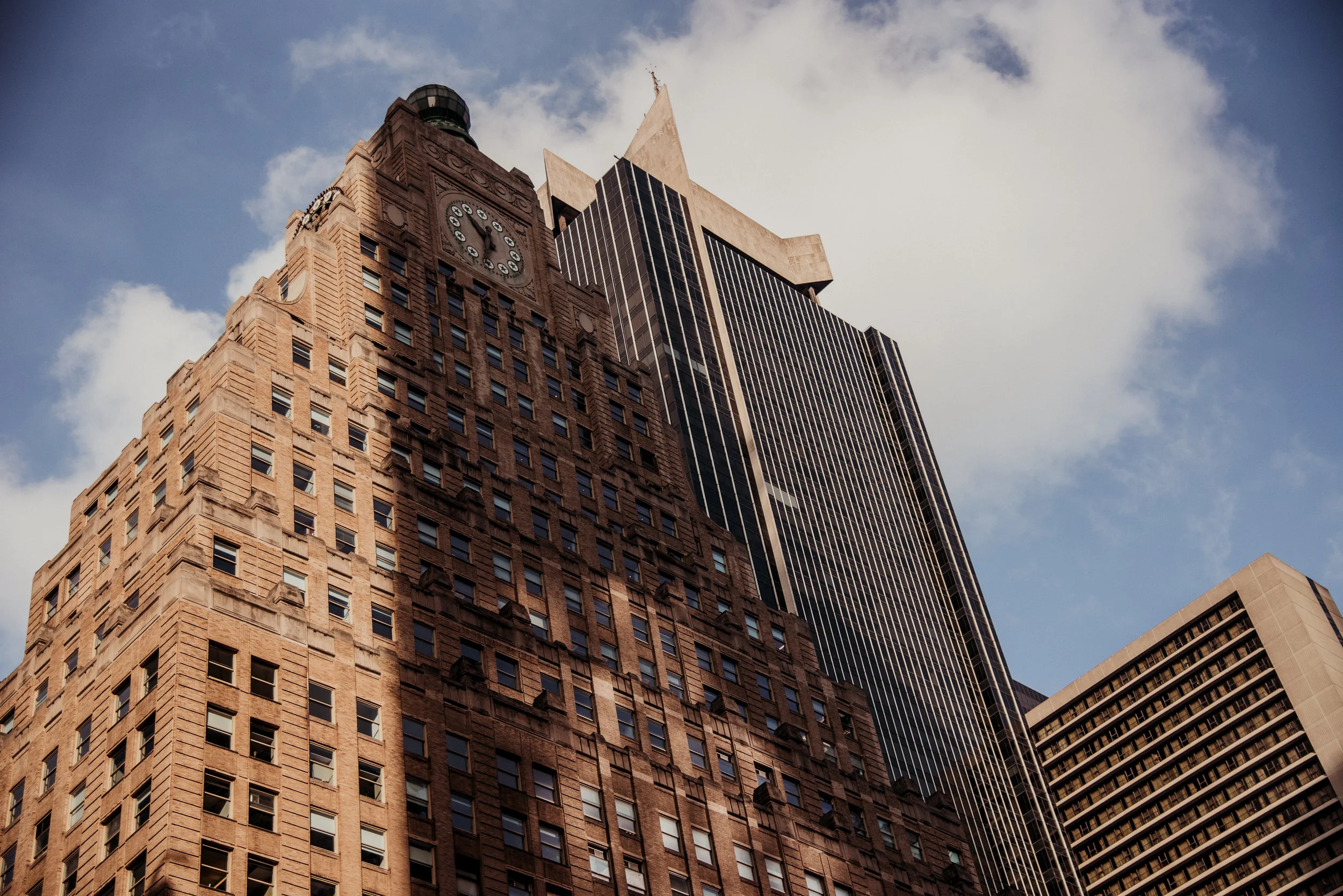 Low-angle view of tall skyscraper buildings with a partly cloudy sky in the background.
