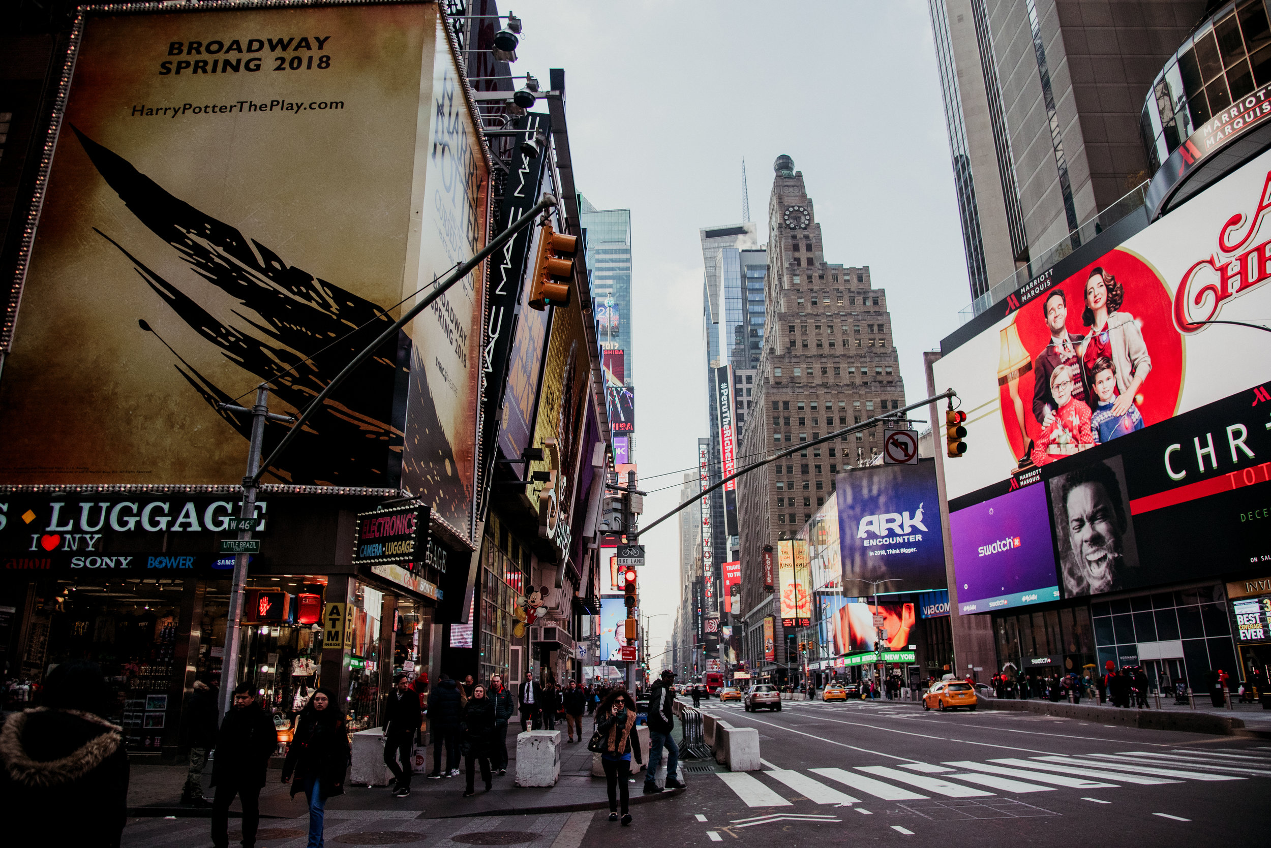 A busy city street in Times Square, New York, with tall buildings, illuminated billboards, and pedestrians crossing the street.
