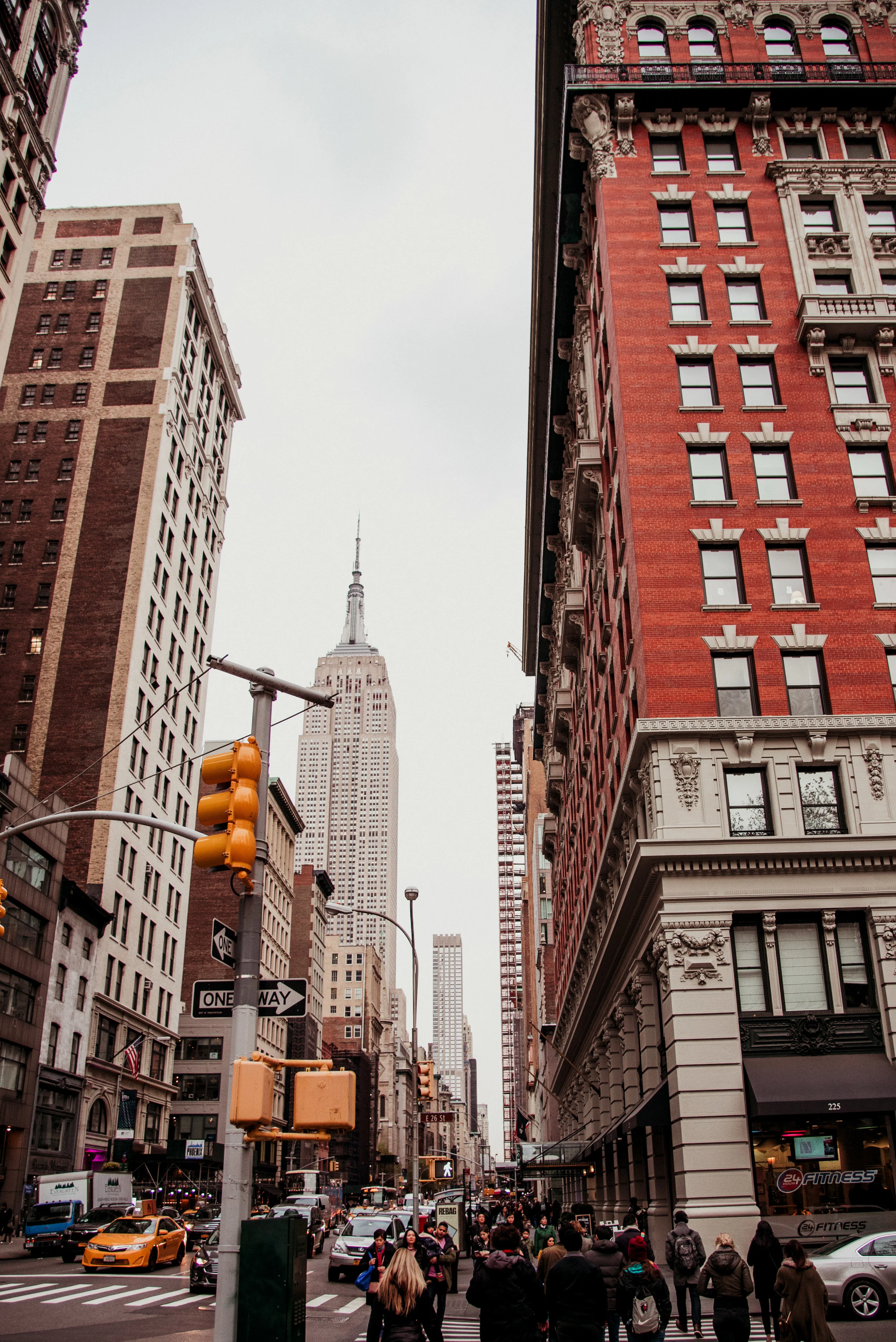 City street scene in New York City with tall buildings, pedestrians crossing the street, and the Empire State Building visible in the background.