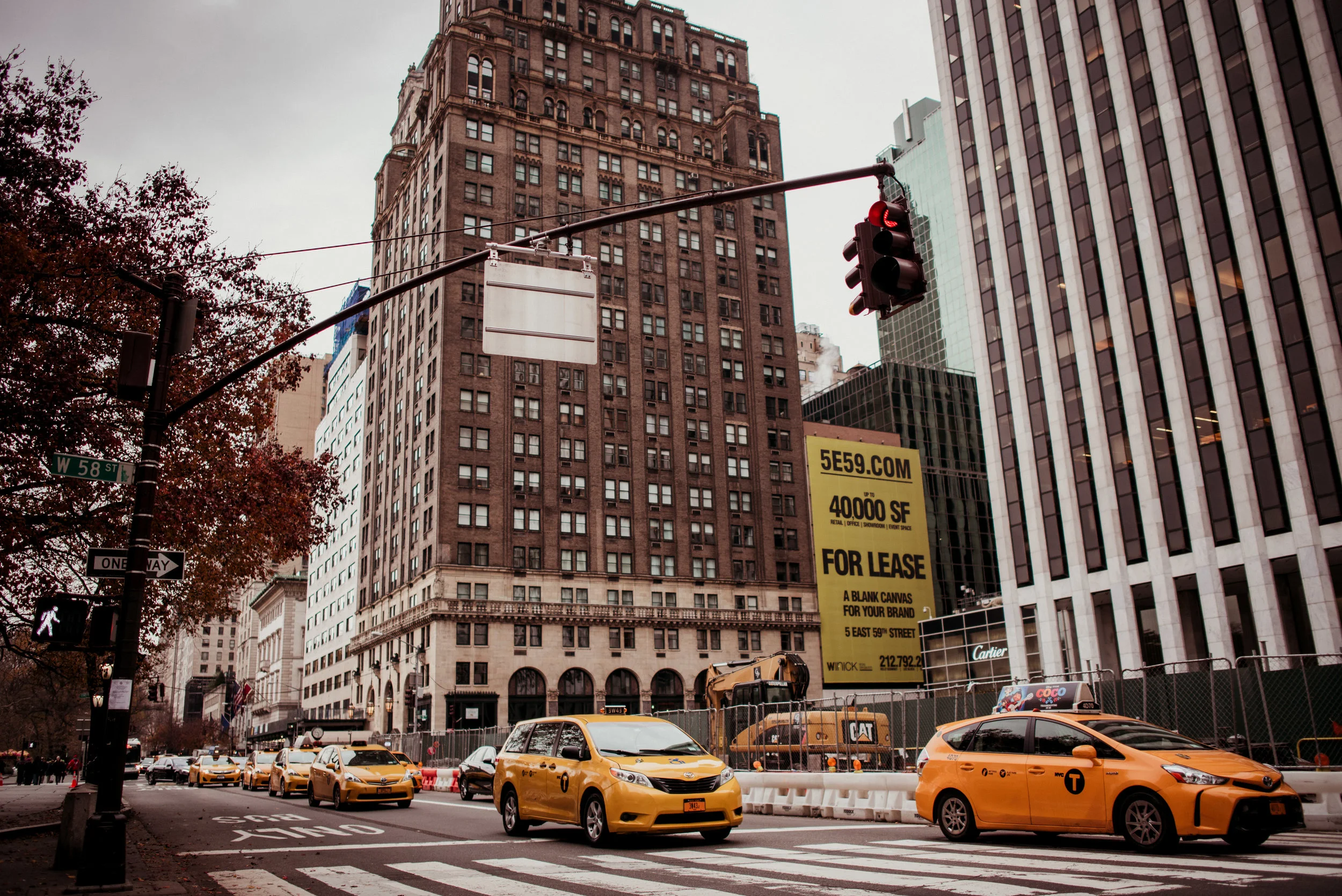 Street scene in New York City with yellow taxis, tall buildings, a red traffic light, and a pedestrian crosswalk.
