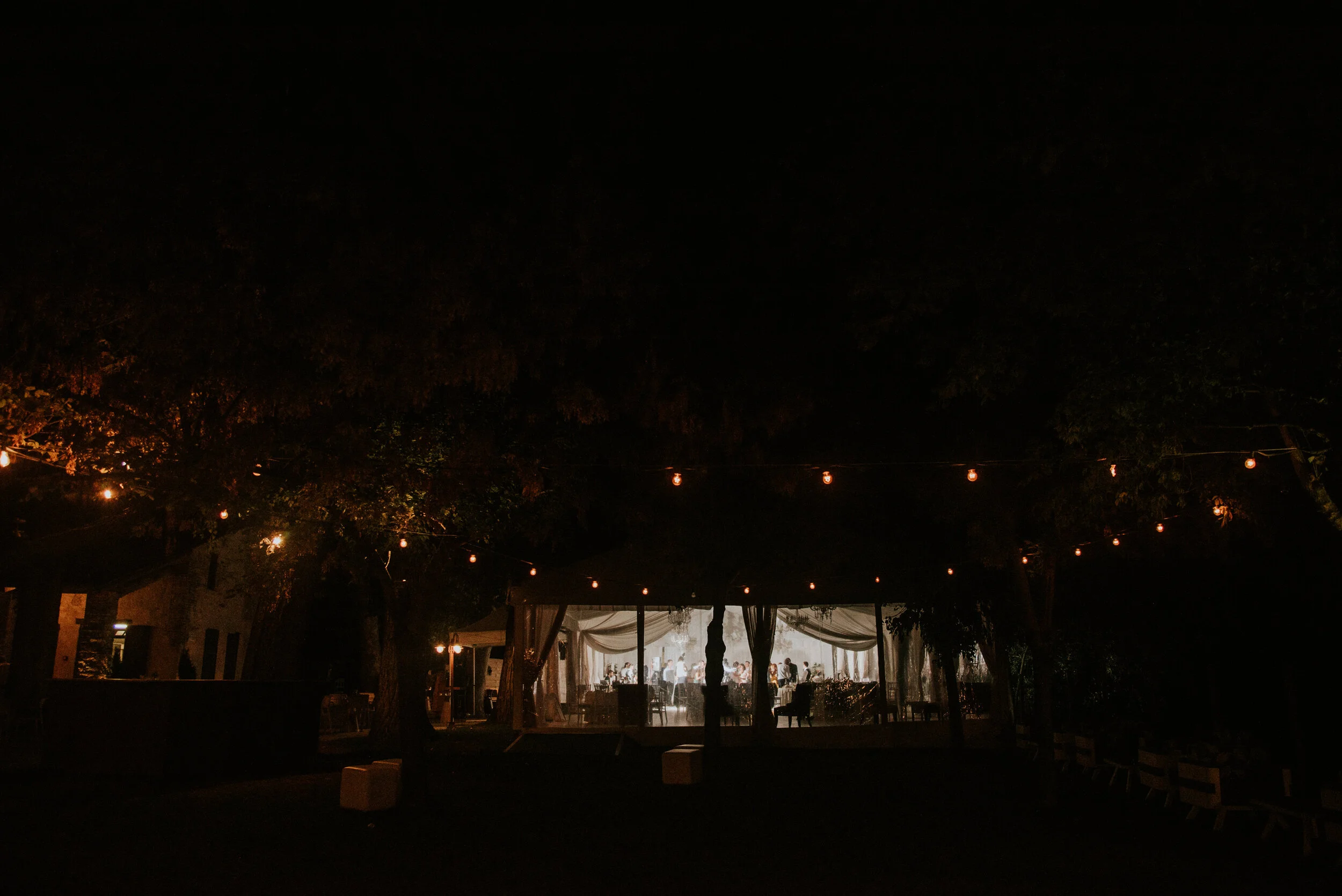 Nighttime outdoor event with string lights and an illuminated tent with people inside.