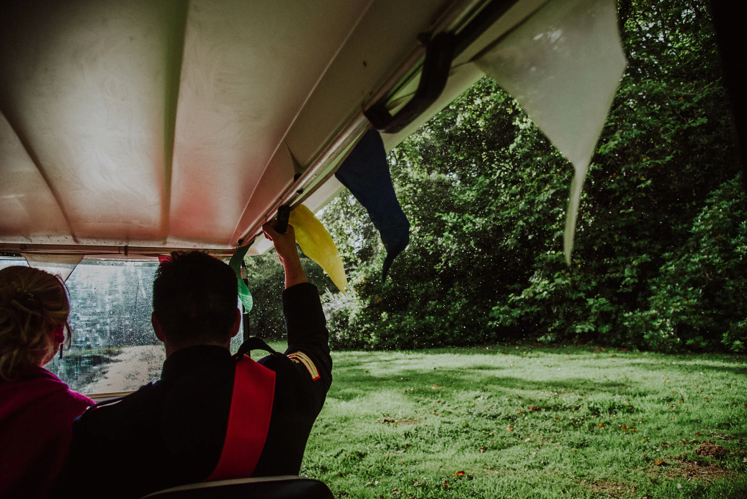 Inside an amphibious tour vehicle, a person is hanging onto a yellow handle, with view of lush green trees and grass through the window.
