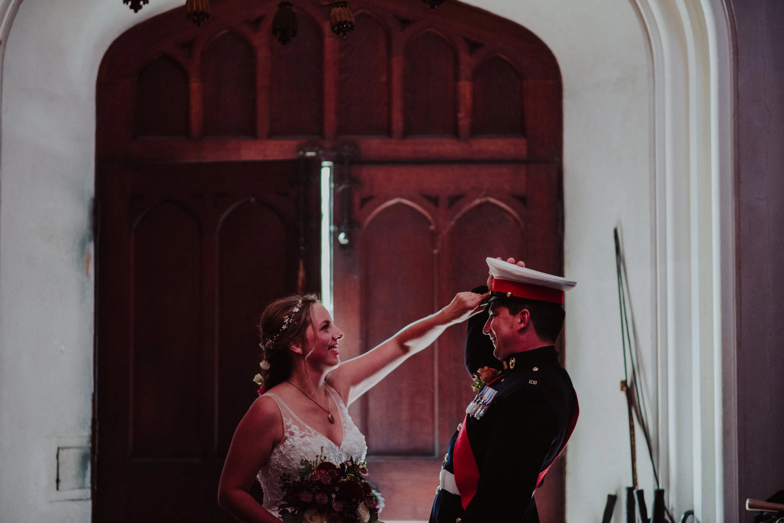 Bride smiling and touching the military groom's hat during their wedding ceremony in a church.