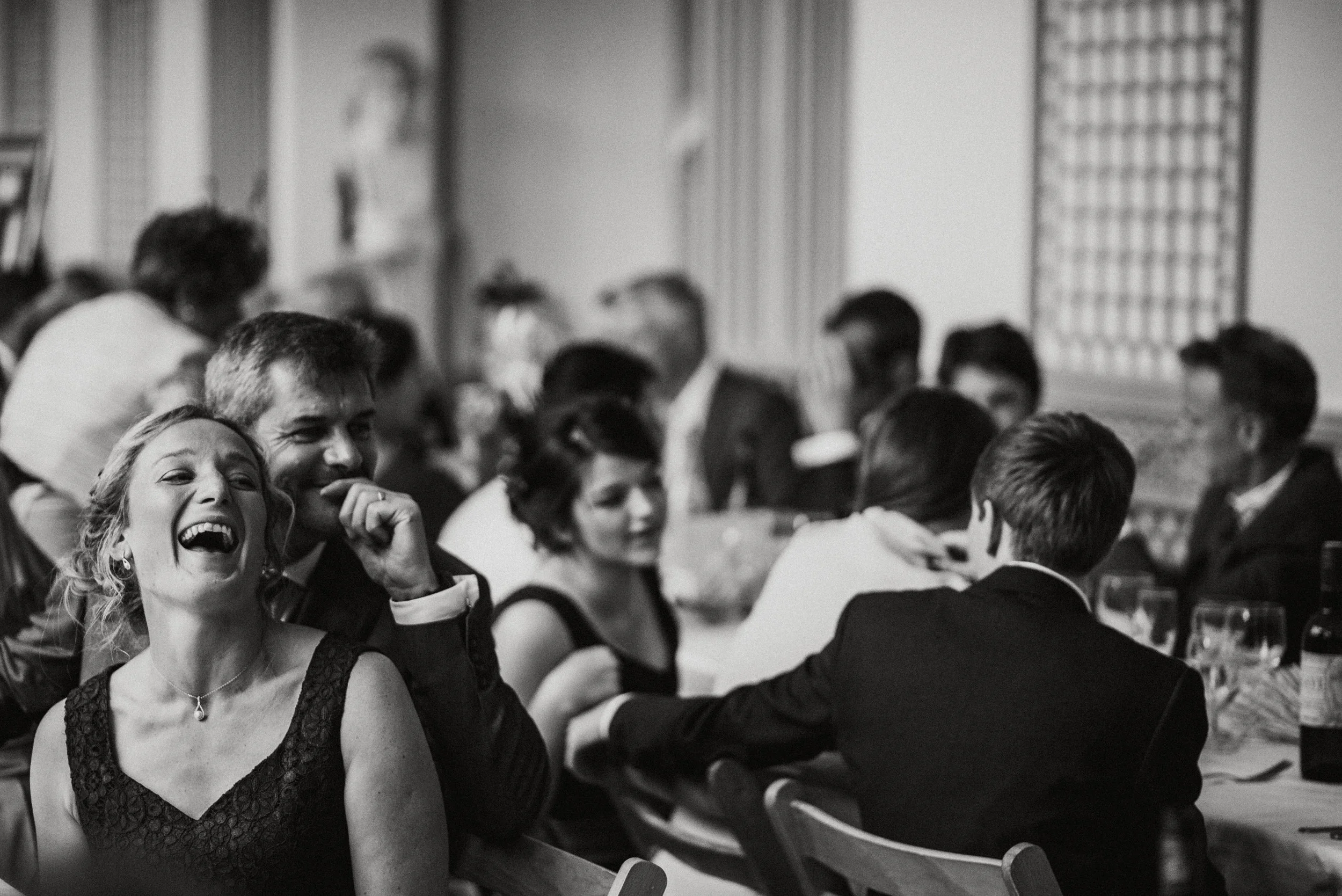 People sitting at a banquet table, some of them laughing and talking, dressed in formal attire, in a decorated room.