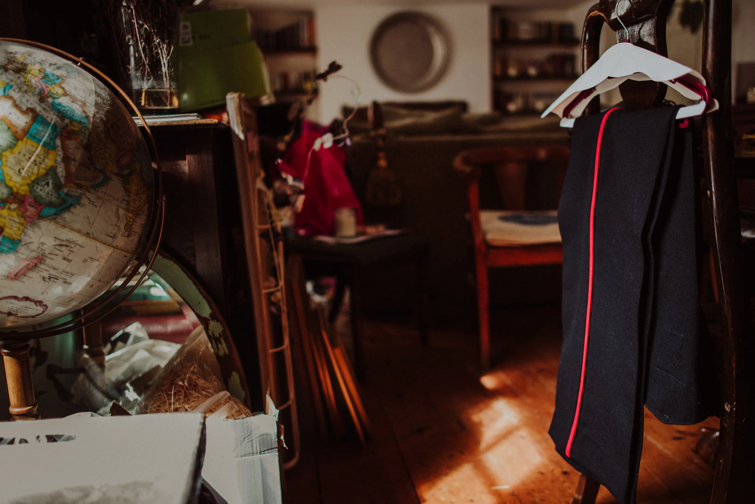 A cluttered room with a globe, stacks of books, and clothing on a chair. Blurred background showing a wooden desk, chair, and shelves.