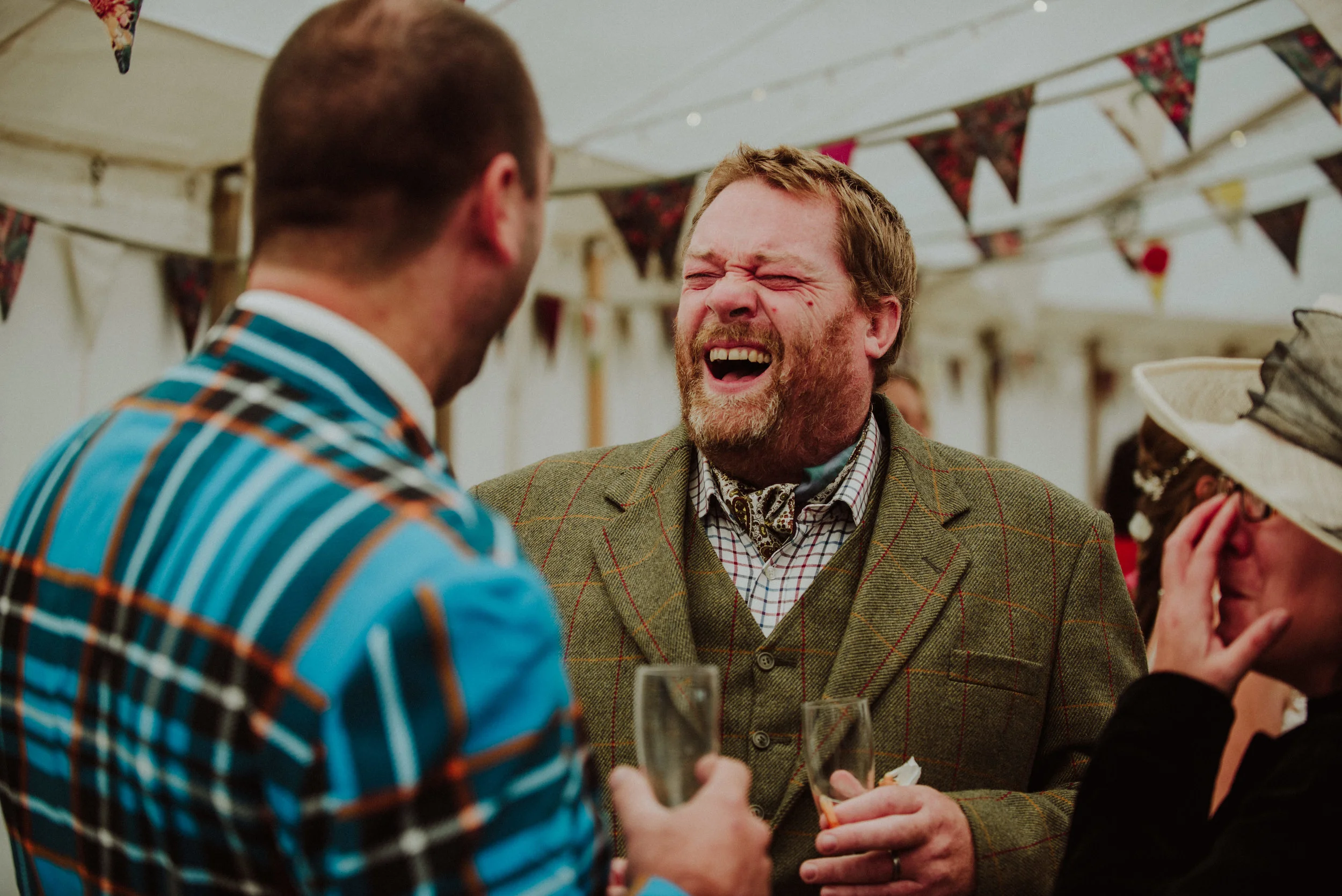 Three people at a celebration, two men and a woman, laughing and chatting under a decorated tent.