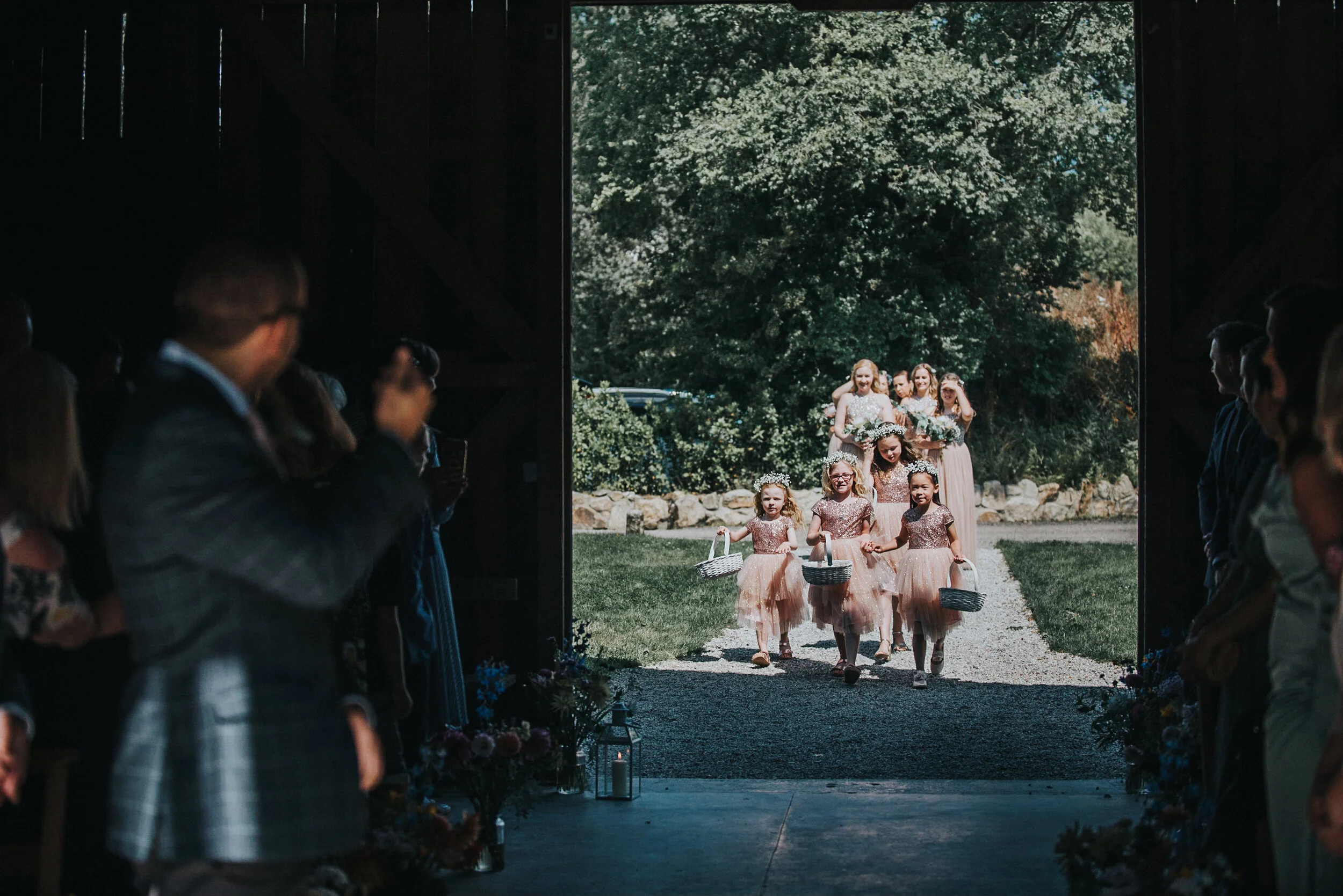 Bridal party entering a wedding venue through a barn door, seen from inside with guests on either side.