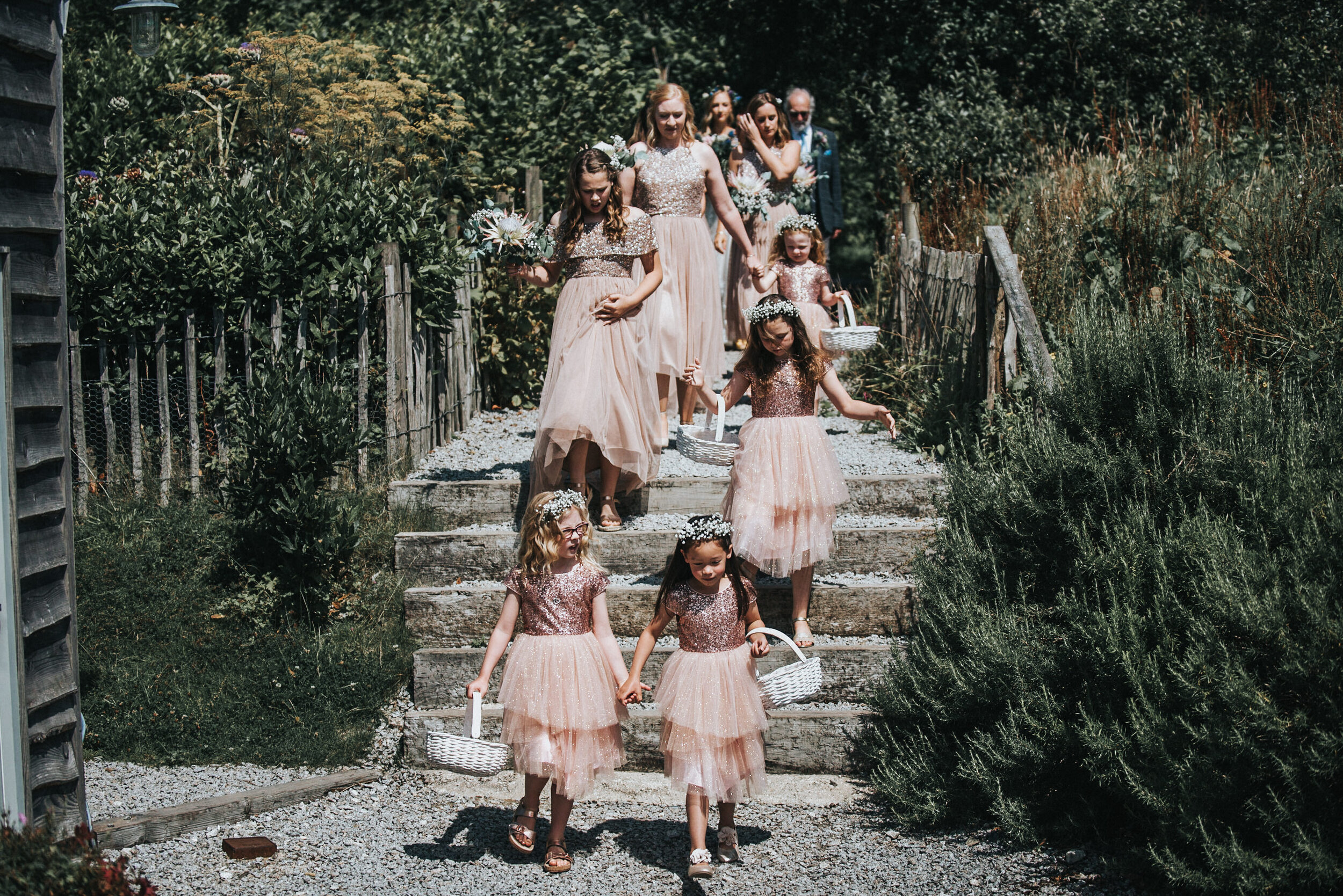 Group of young girls and adults dressed in formal attire walking down outdoor stone steps during a wedding or special event.