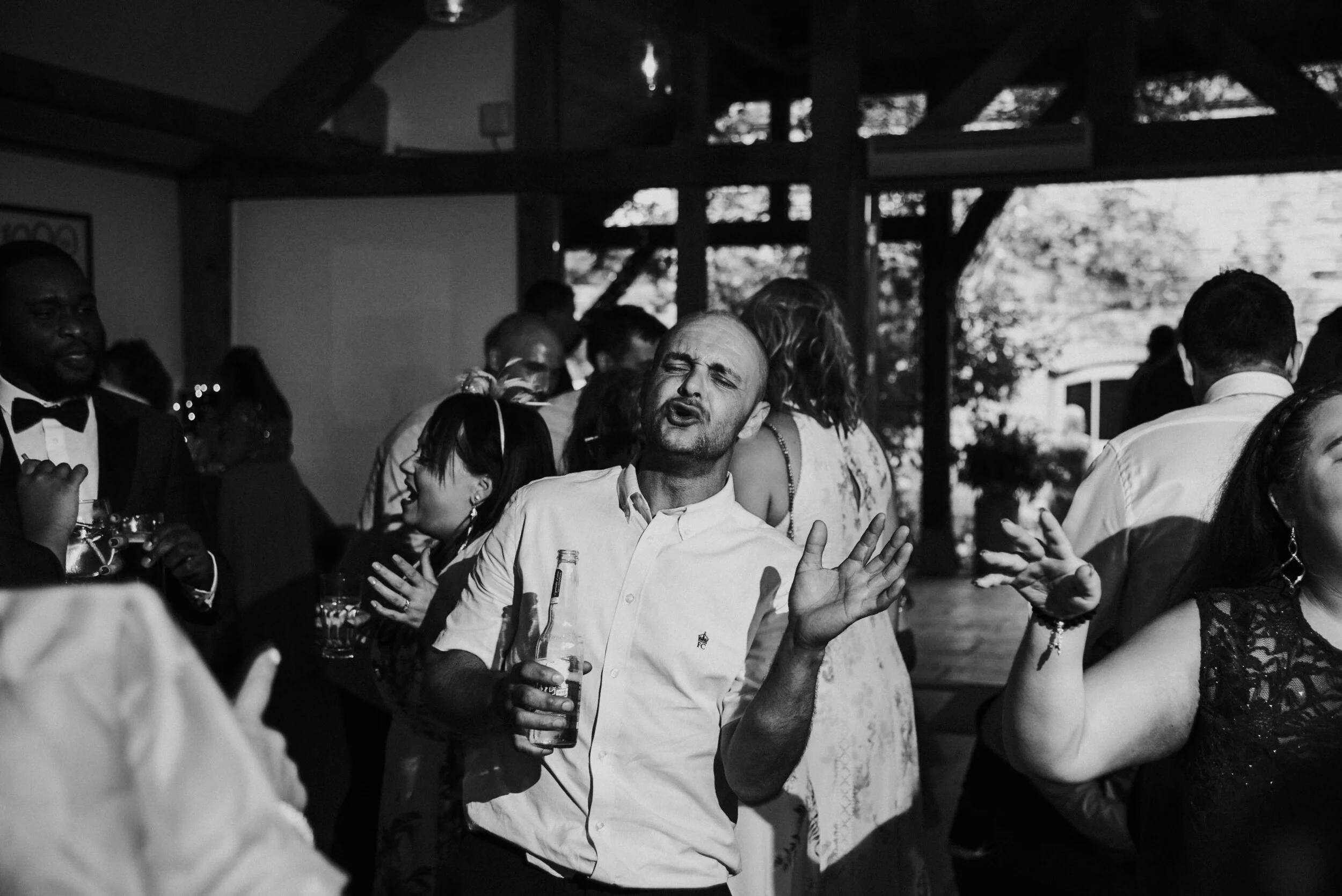 People dancing and socializing at a party or celebration, with a man singing or speaking into a microphone in the center.