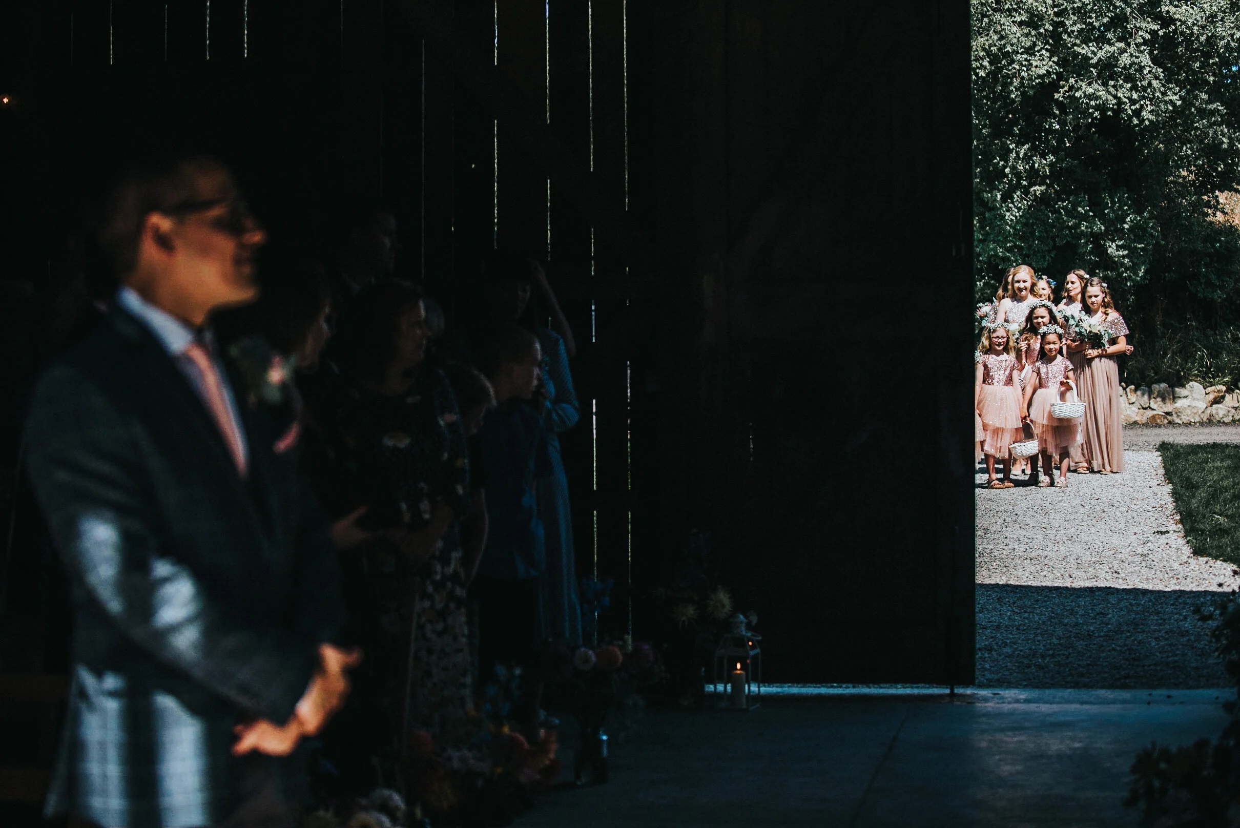 A group of people, mostly women and children, gathered outside in daylight, seen through a dark opening, with a lush green background.