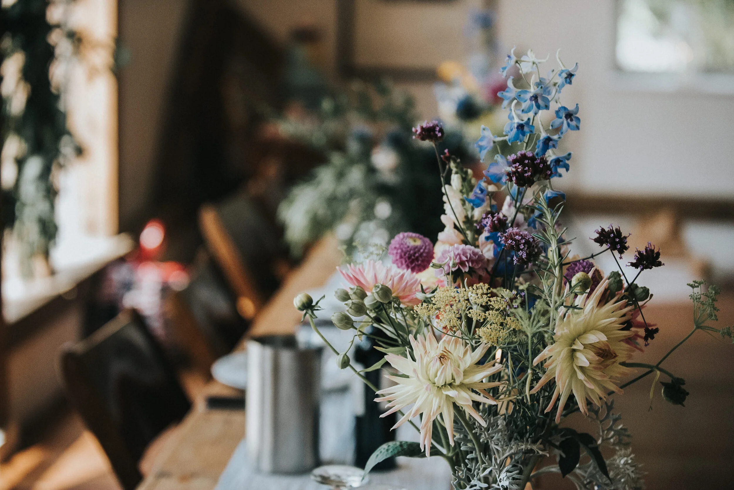 A bouquet of various colorful flowers on a table, with blurred people in the background.