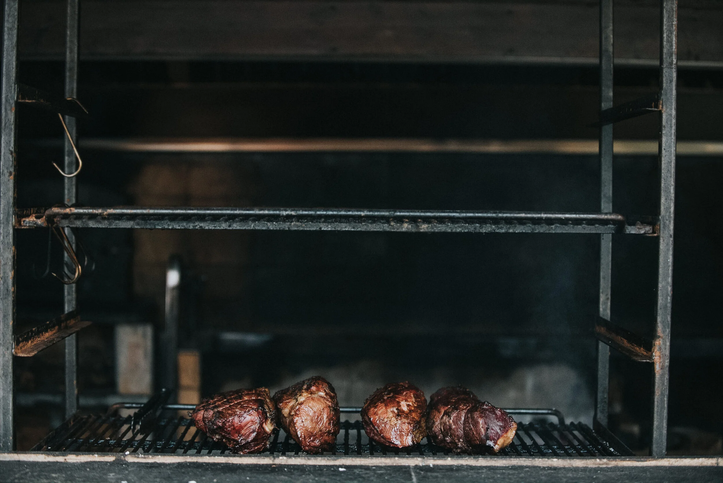 Four cooked pieces of meat on a grill inside a barbecue smoker.
