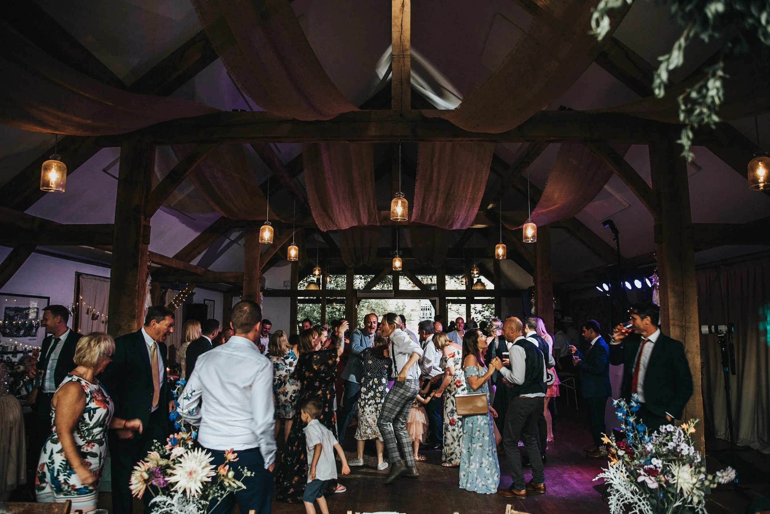 People dancing and socializing at a party inside a rustic venue with wooden beams and dim lighting.