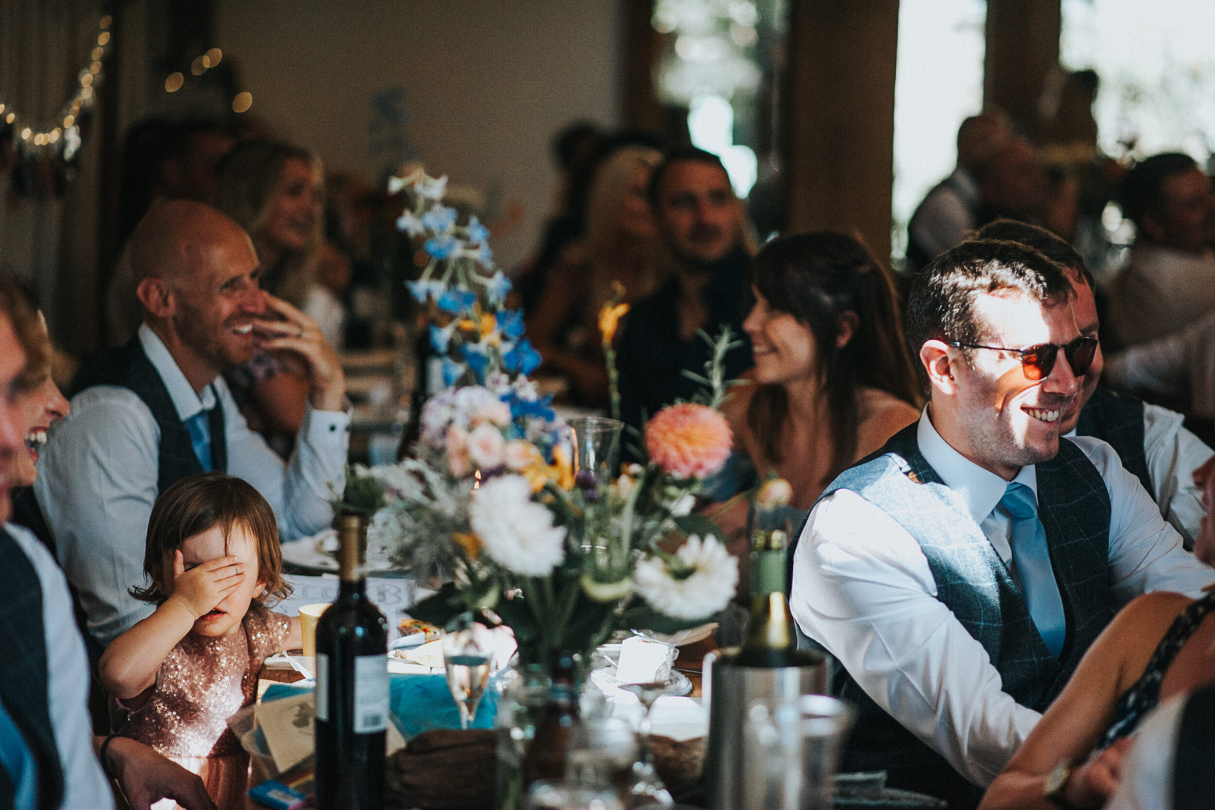 People sitting at a decorated dining table, laughing, enjoying a celebration with flowers and drinks.