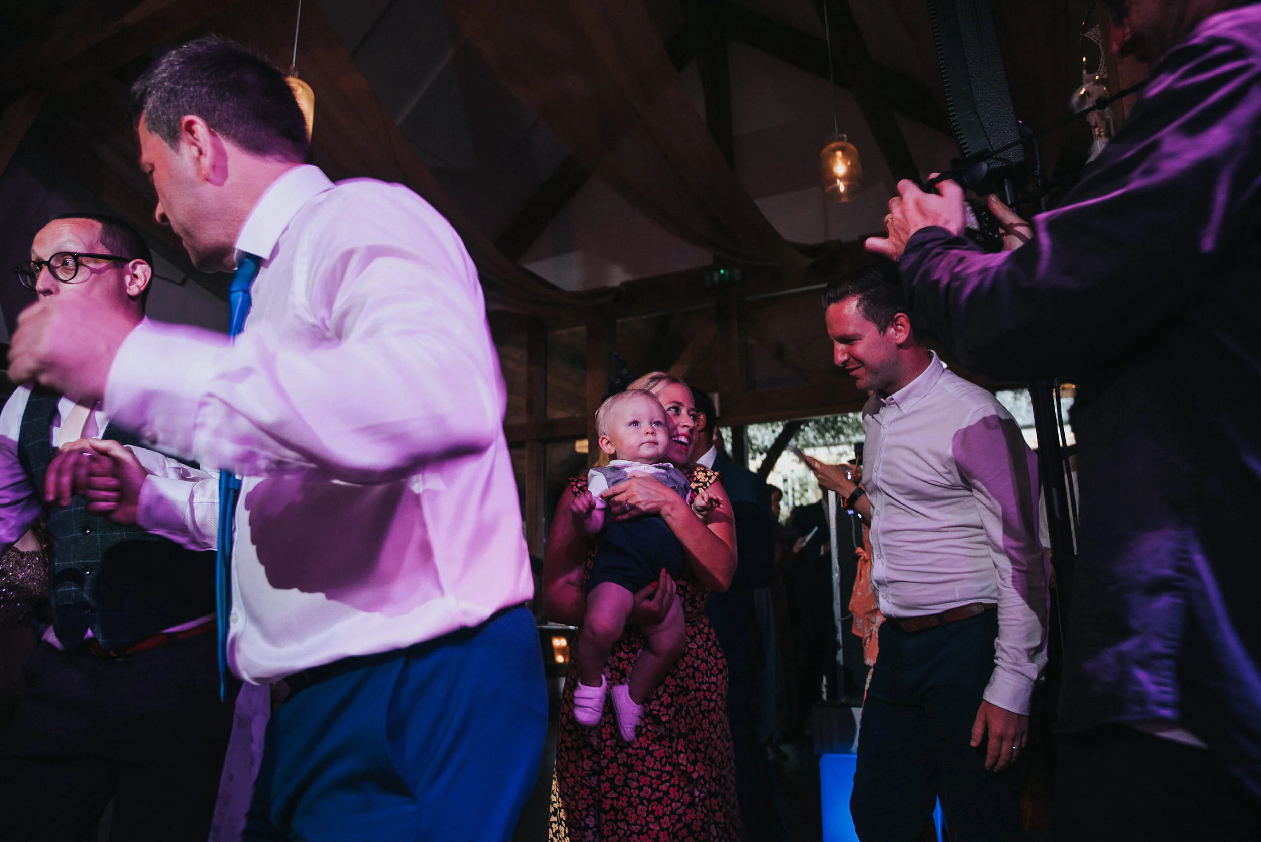 People dancing and celebrating at a party or wedding reception with a woman holding a child and a man smiling.