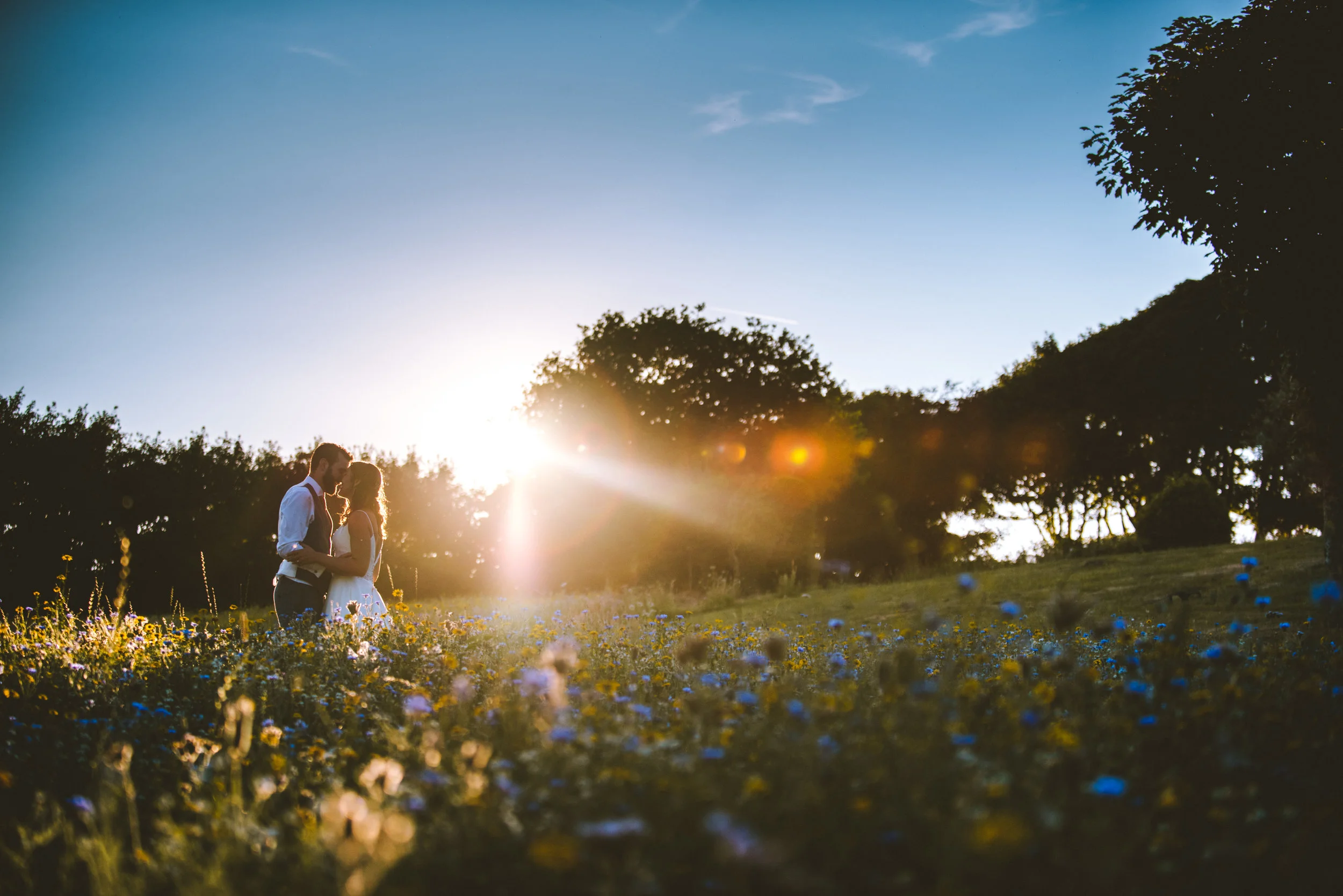 A couple standing close together in a field of flowers at sunset, sharing an intimate moment.
