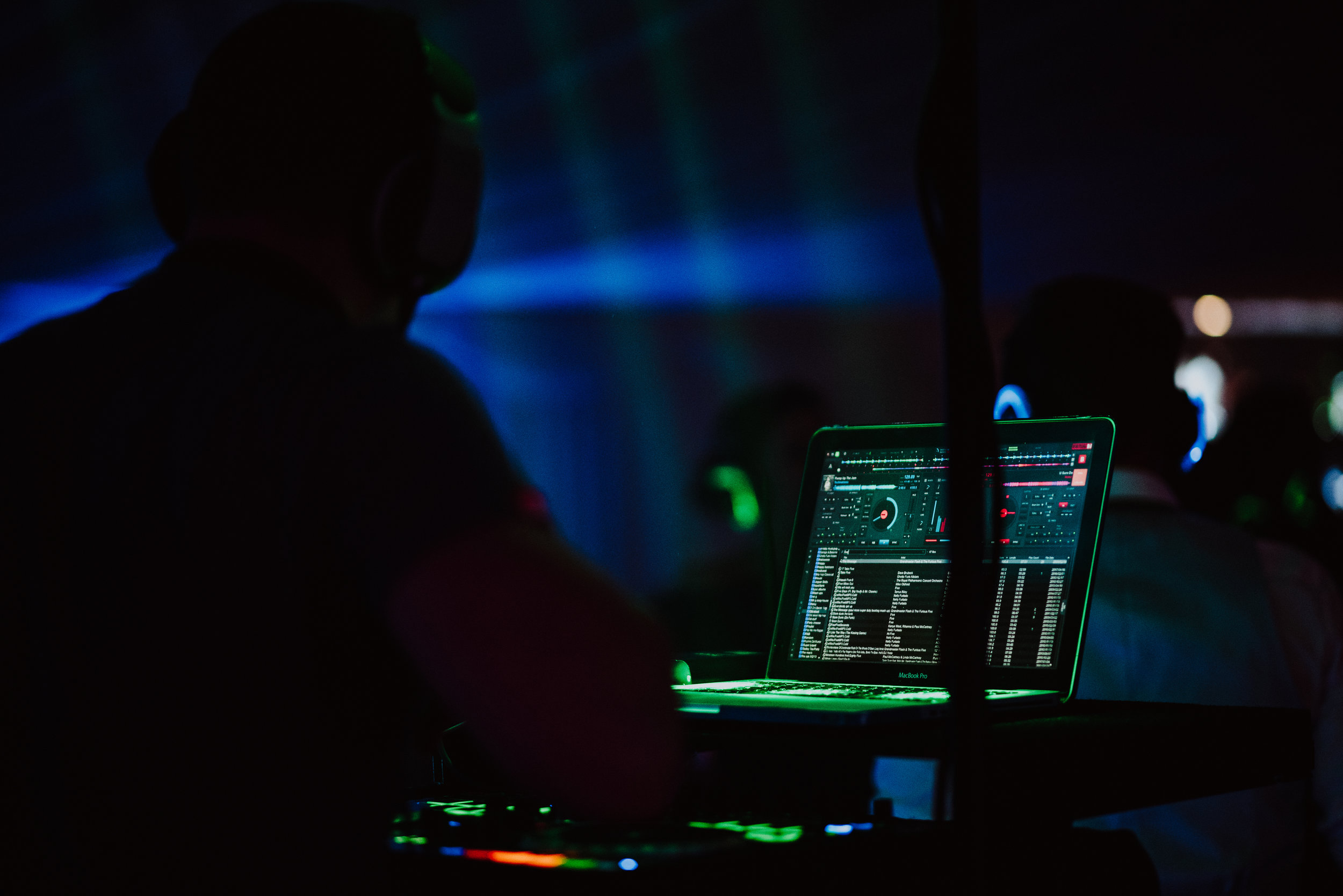DJ using a laptop with a music mixing software in a dark club or party setting.