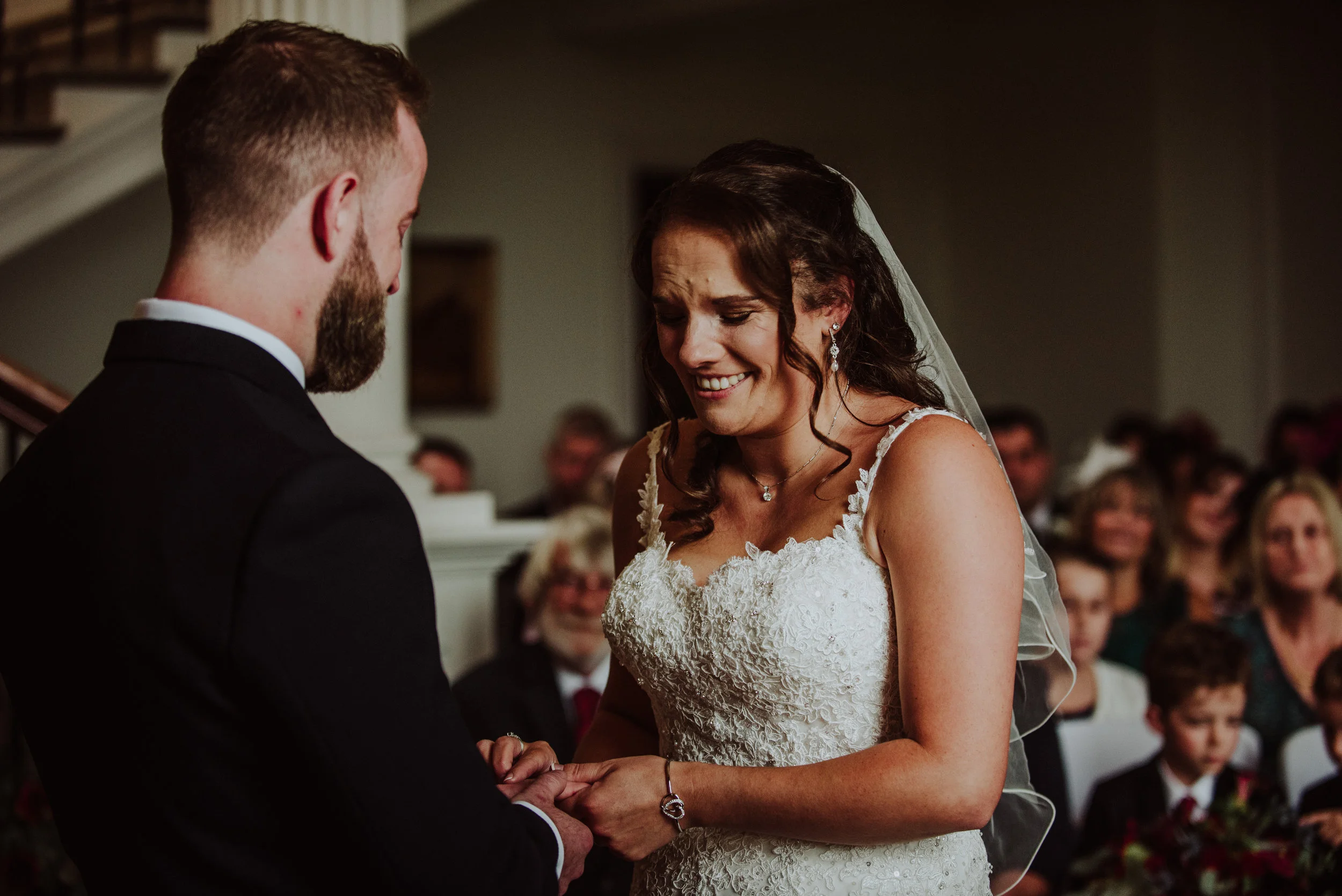 Bride and groom exchanging wedding vows indoors, with guests observing in the background.