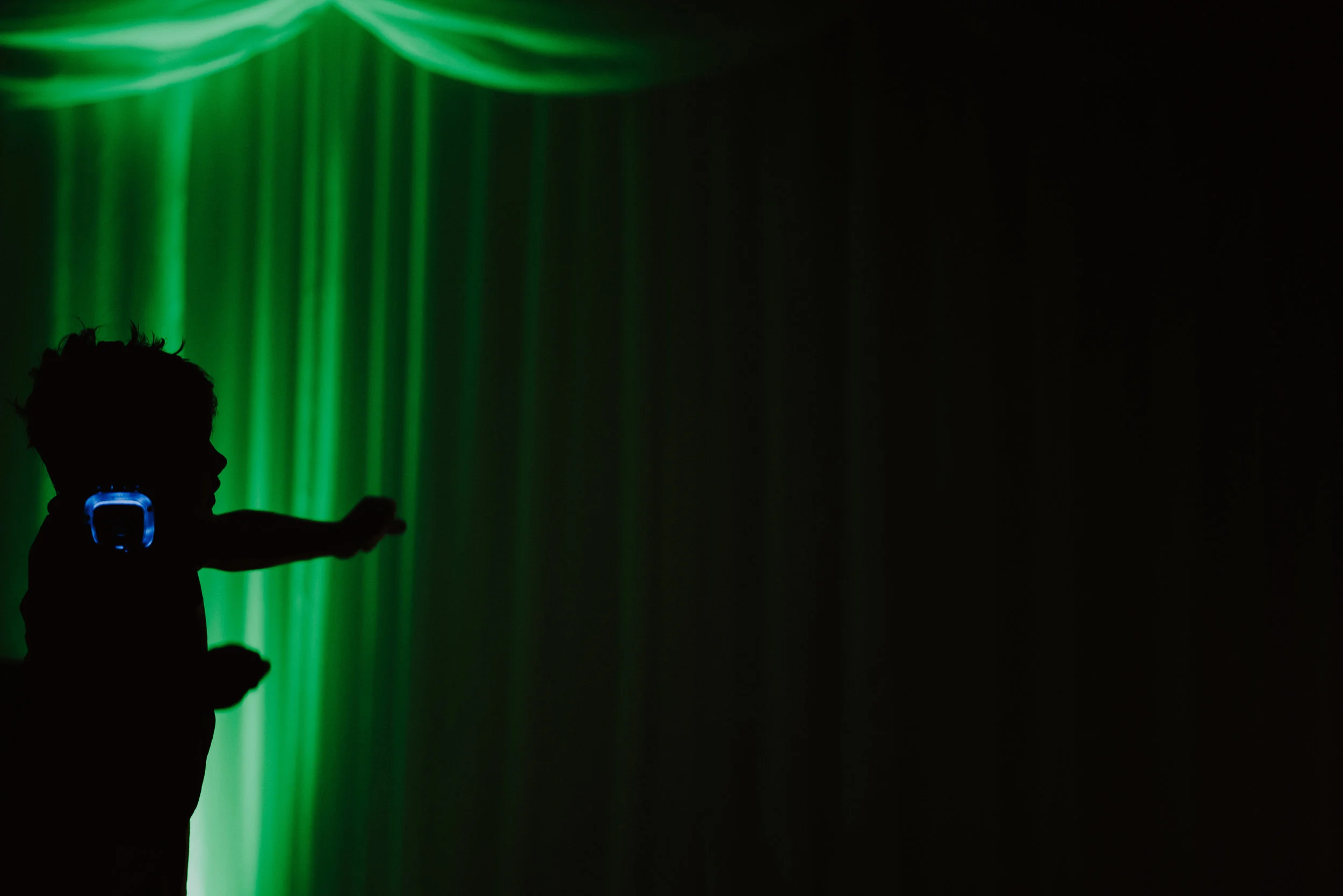 Silhouette of a child with headphones reaching towards green and black background lights.