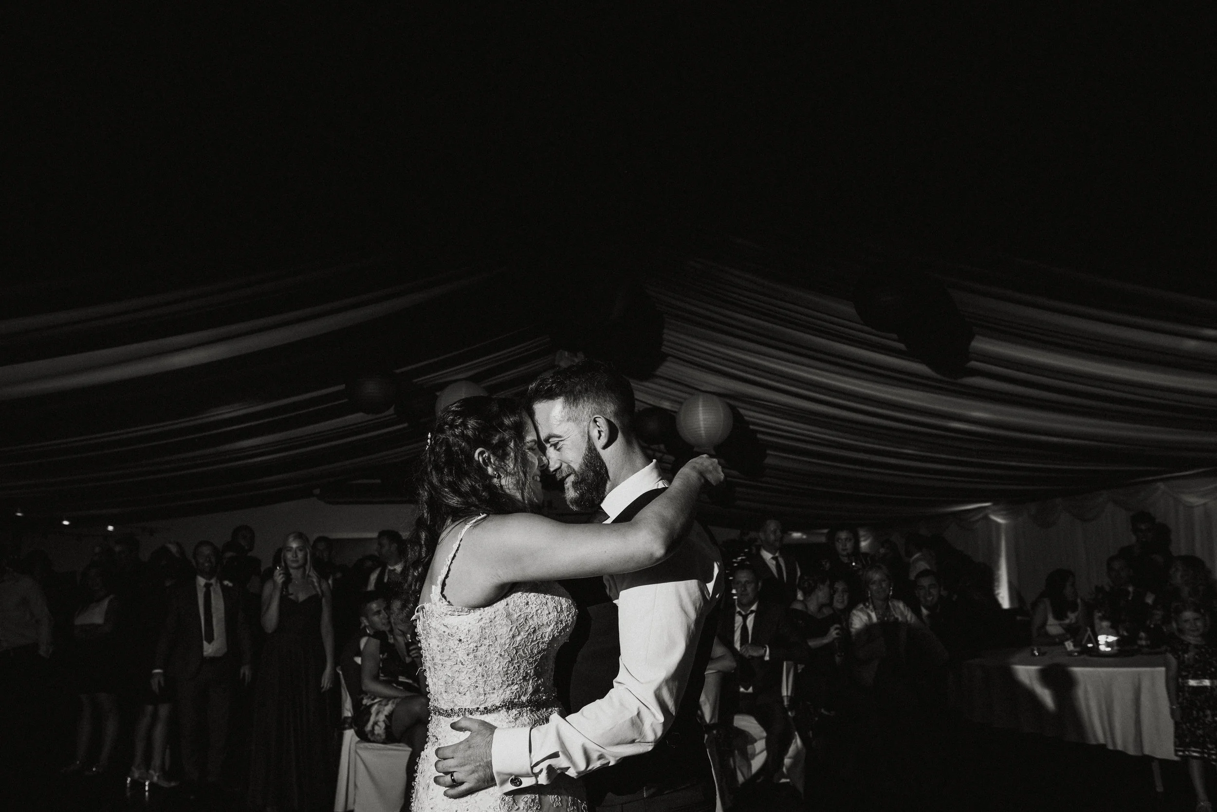 A bride and groom sharing their first dance at a wedding reception, surrounded by seated guests and decorated with hanging paper lanterns.