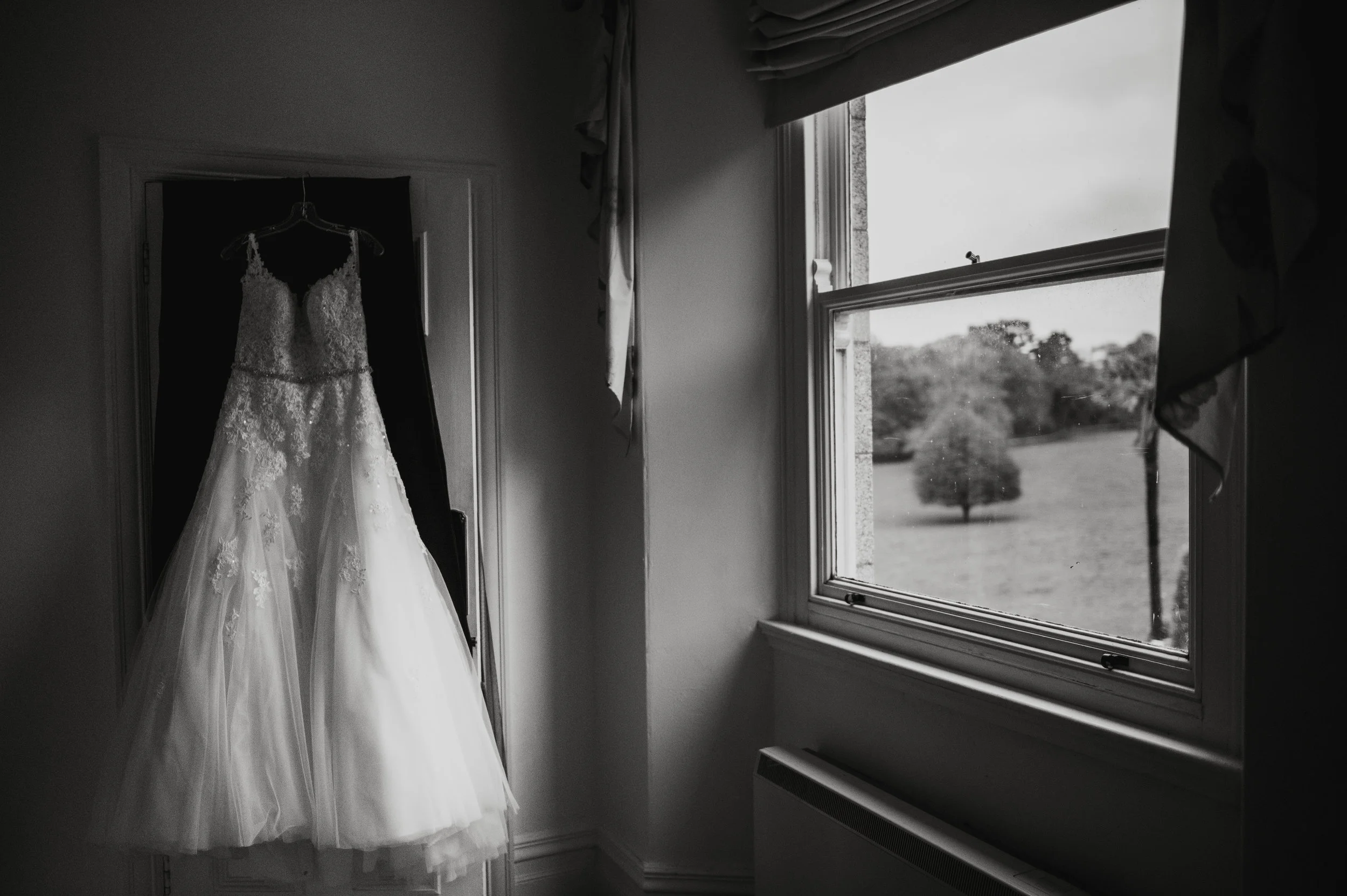 A wedding dress hanging on a closet door with an open window showing a grassy landscape outside.