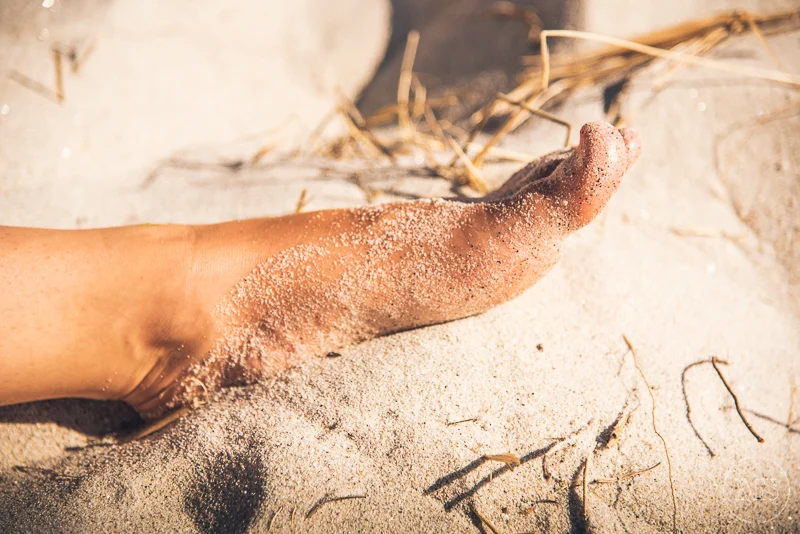 A human hand resting on sandy ground with some scattered twigs nearby.