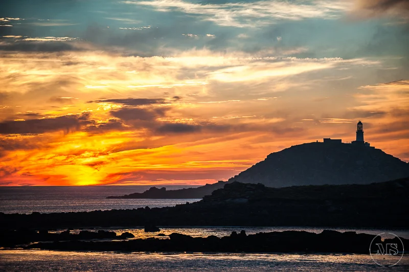Isles of scilly photography. Sunset over the ocean with a lighthouse on a hill in the distance.