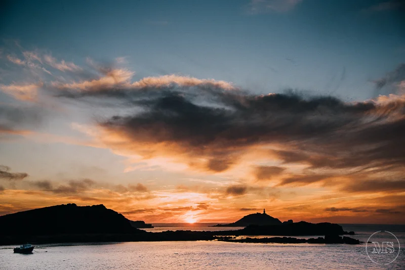 Sunset over a body of water with silhouette of hills and a lighthouse in the distance - Isles of Scilly Professional Photographer - Mark Shaw Photography 