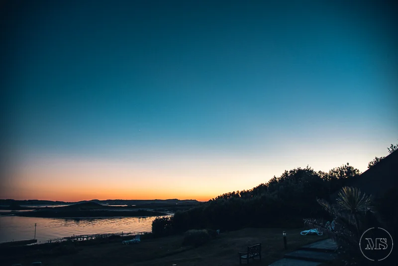 A serene sunset or sunrise over a body of water with a silhouette of trees and some hills in the background.