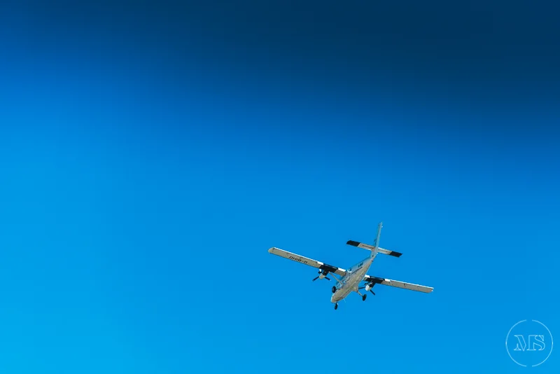 Isles of scilly photography. A white and blue aircraft flying in a clear blue sky.