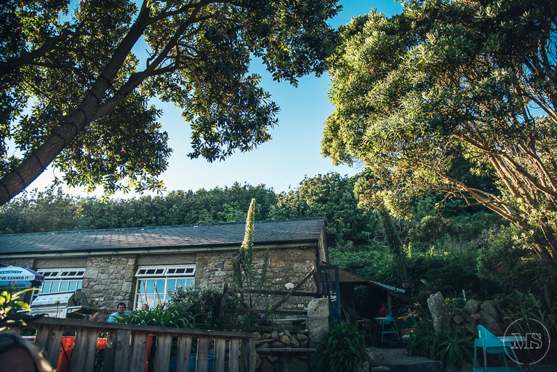 Isles of scilly photography. A stone house surrounded by trees and greenery under a clear blue sky.