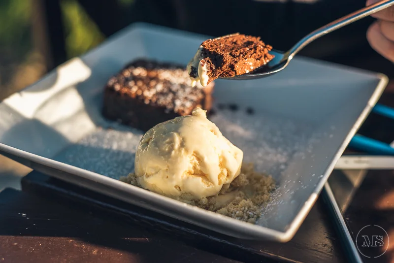 Scooping chocolate cake with a spoon, served with vanilla ice cream on a white plate