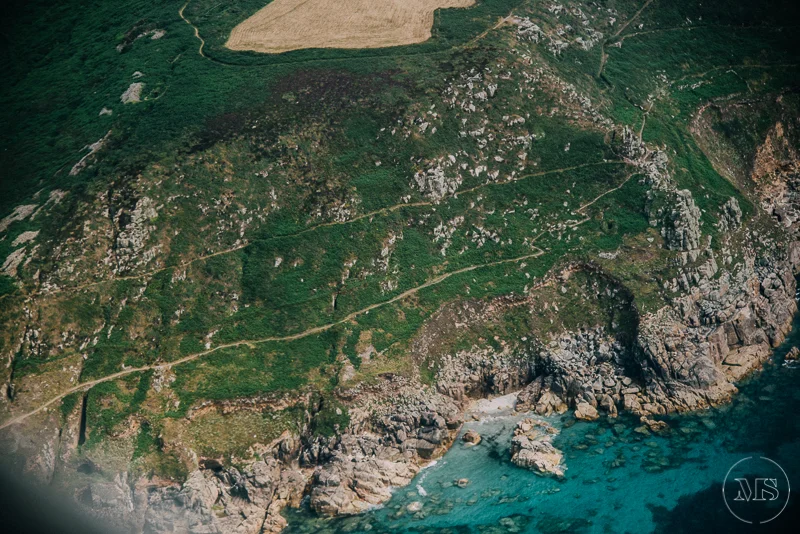 Aerial view of a rocky coastline with blue ocean water and green hills.