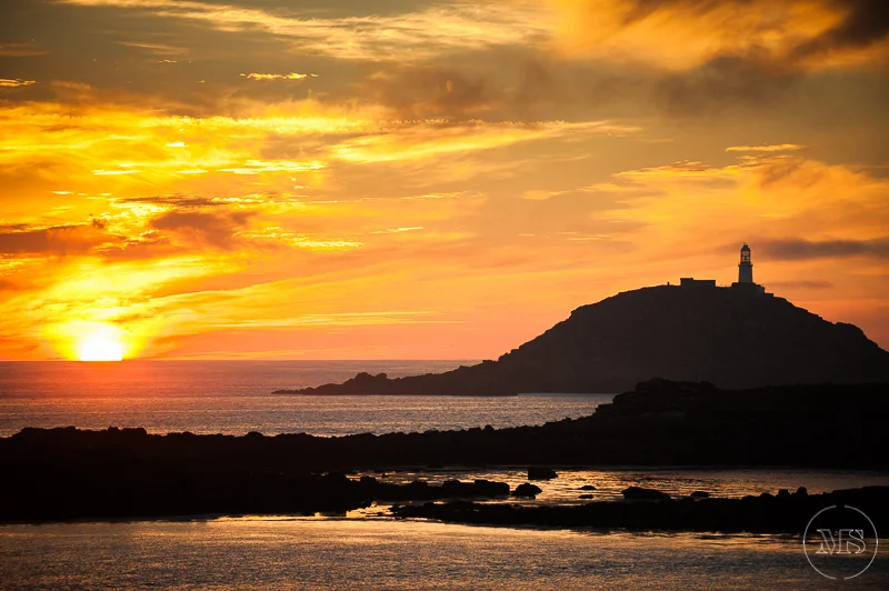 Isles of scilly photography. Sunset over the ocean with a lighthouse on a hill in the background.